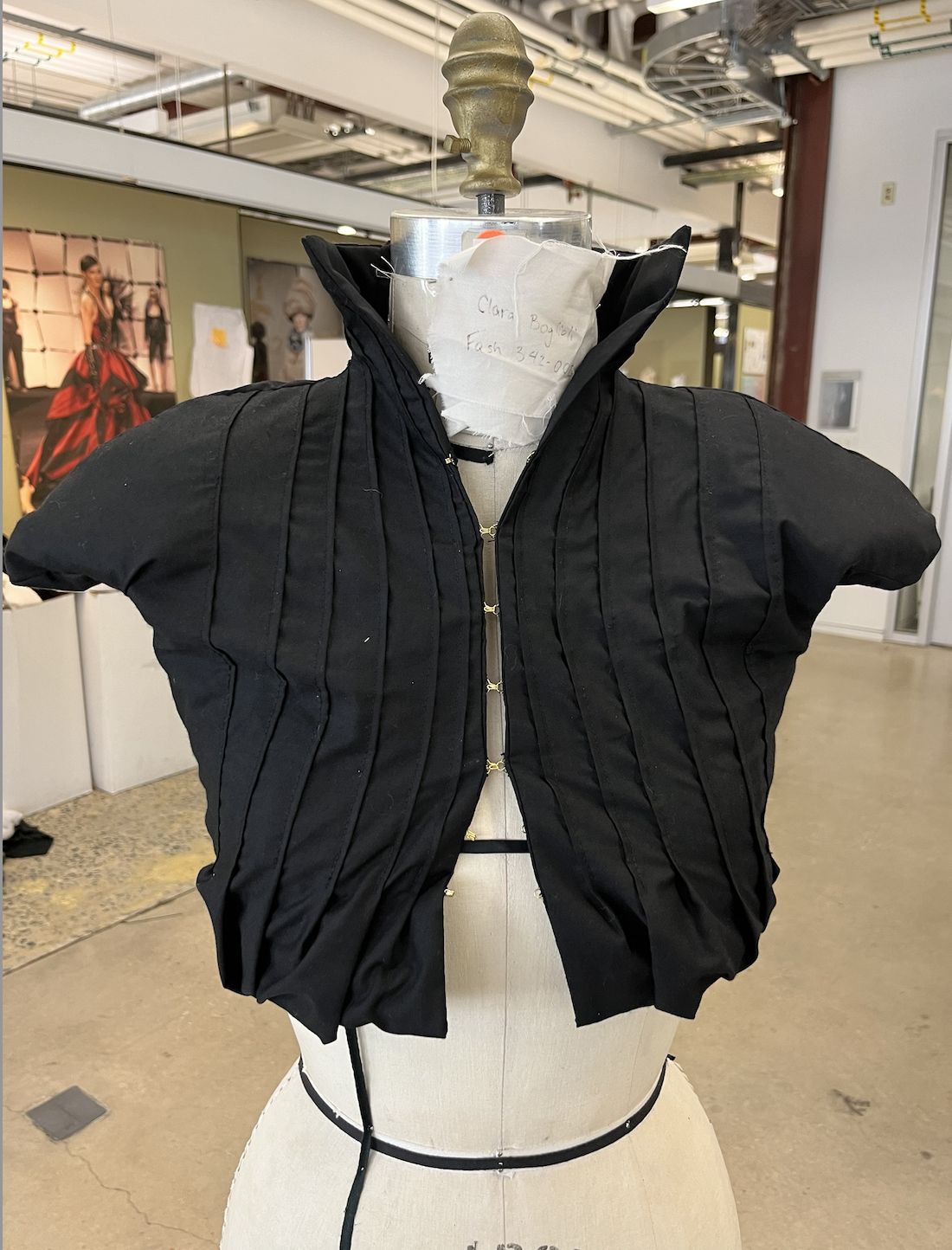 Cropped pleated jacket with bubble hem, high collar hitting at the jawline, shoulder pads, and gold hook and eye closures all along the front.