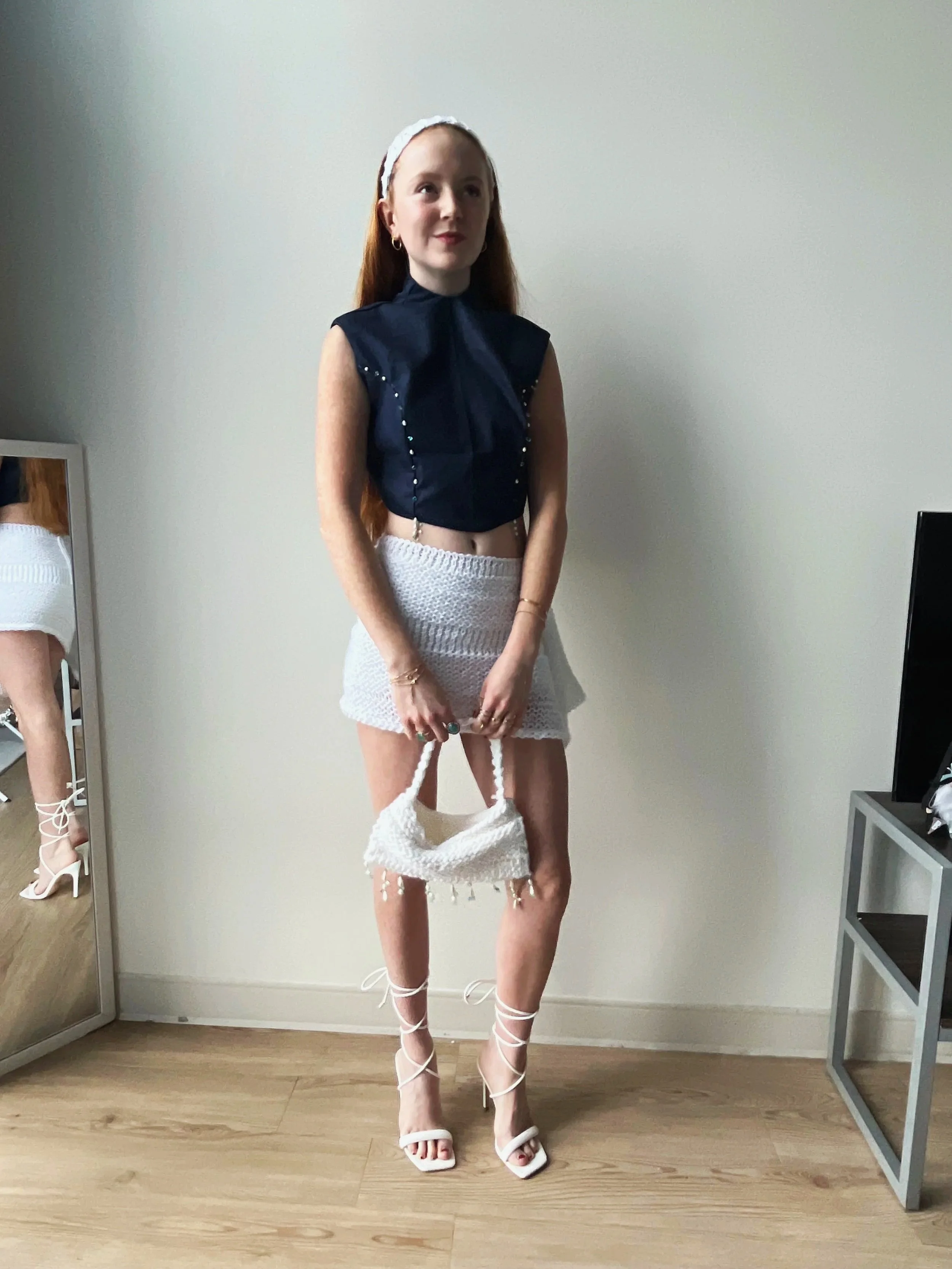 High-neck top with corset-style back closure and beaded embroidery. Hand-knit mini skirt, headband, and purse with beaded embroidery. Made with denim fabric, acrylic yarn, gold grommets, and glass beads.