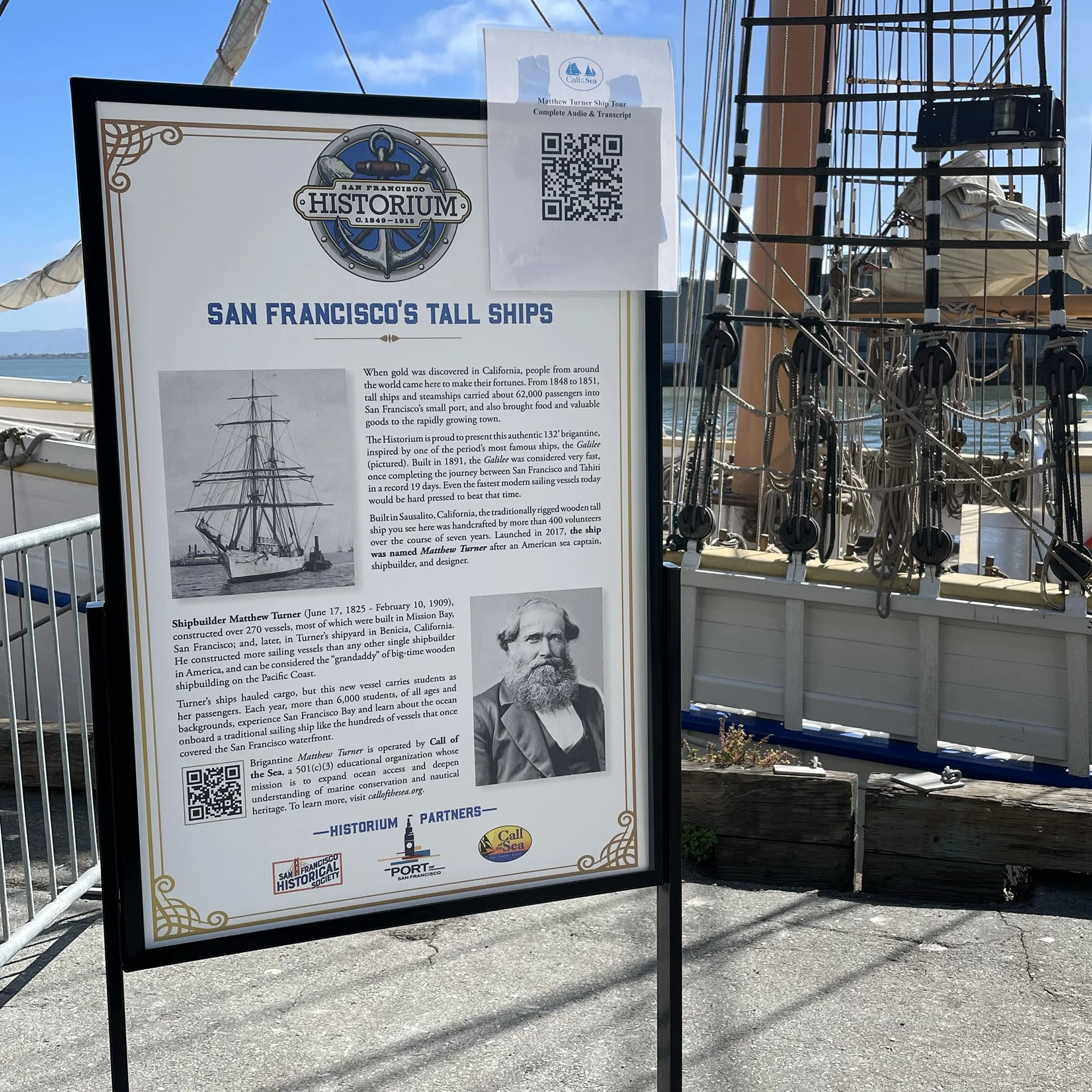 Information board about San Francisco's tall ships and Matthew Turner ship tour, with a black and white portrait of Matthew Turner, a QR code, and logos of local maritime organizations, set against the background of the San Francisco waterfront and a wooden ship rigging structure.