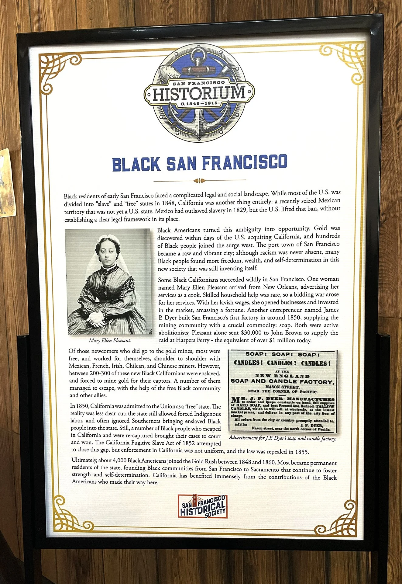 A framed informational display titled 'Black San Francisco' with a black and white photograph of Mary Ellen Pleasant and a newspaper advertisement for soap and candles from the 1800s. The display is from the San Francisco Historical Society.