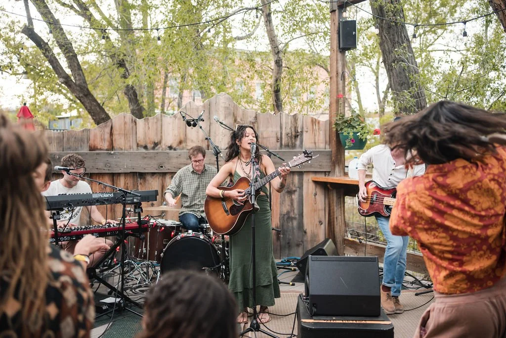 Thylan singing and playing guitar while a band performs outdoors in a backyard with string lights and trees.