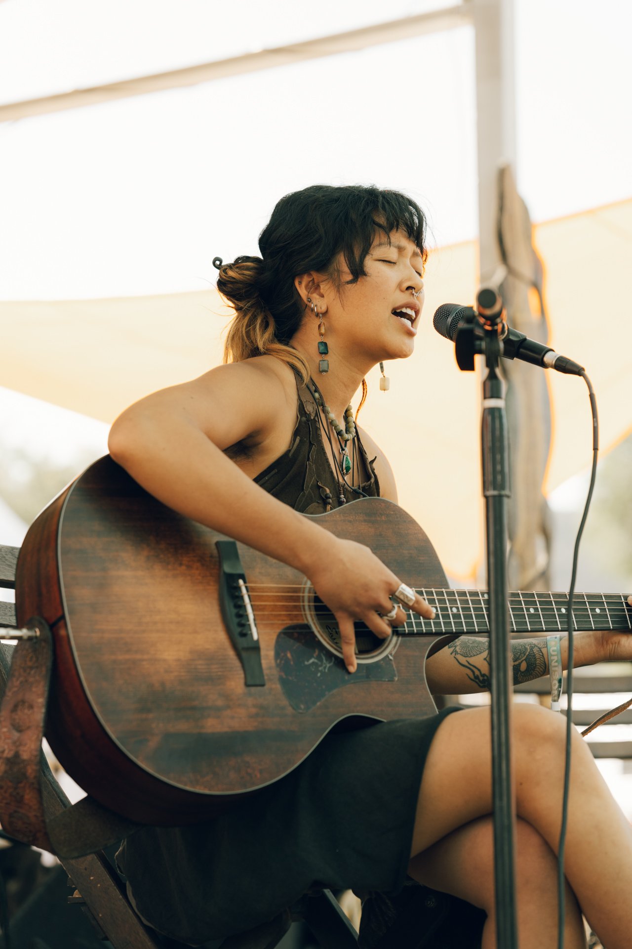 Thylan, online vocal coach, playing an acoustic guitar and singing at Unison Festival outdoors.