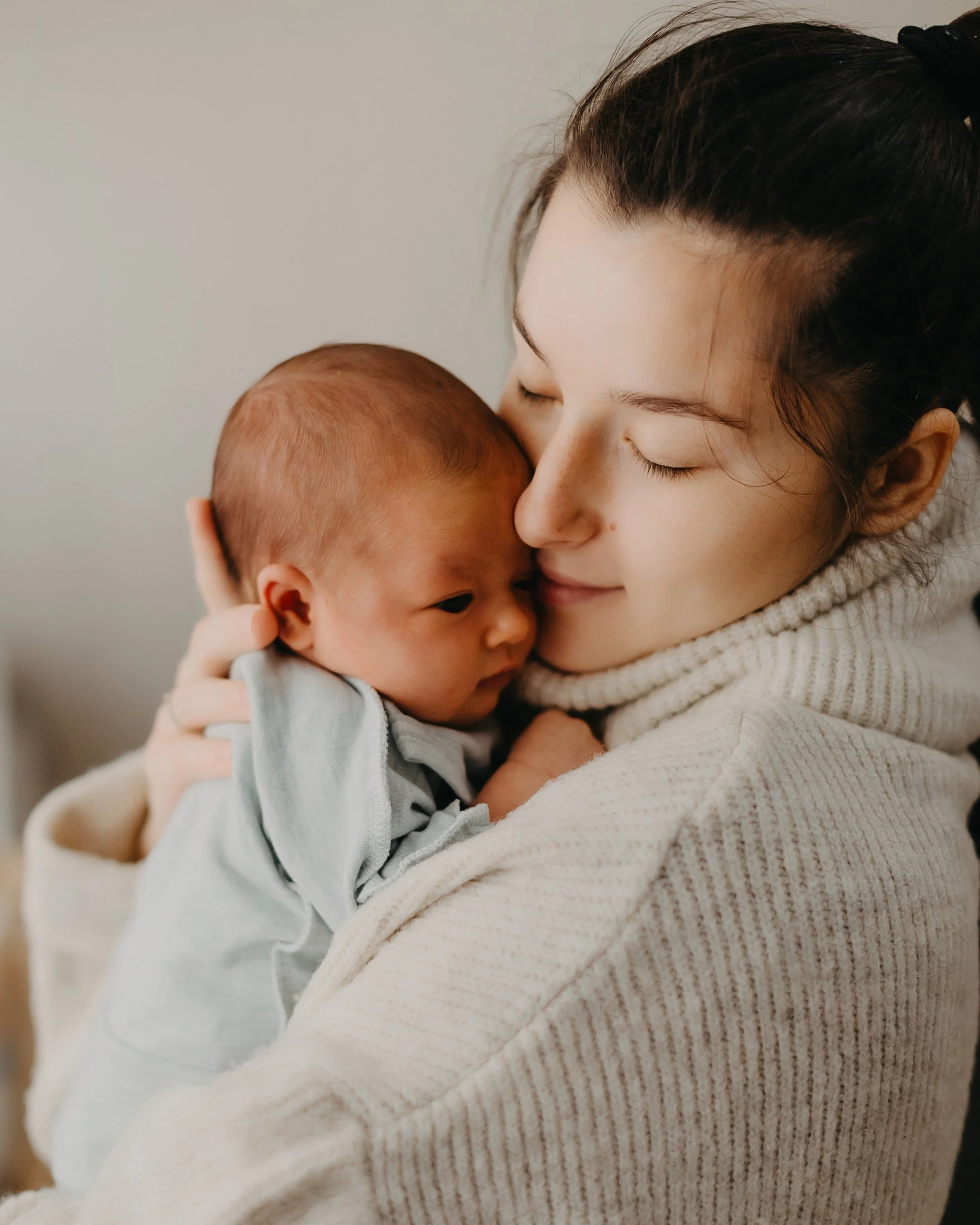  Mother holding her newborn cheek to cheek with eyes closed in a tender postpartum bonding moment, representing the emotional and physical connection that supports feeding and weight gain