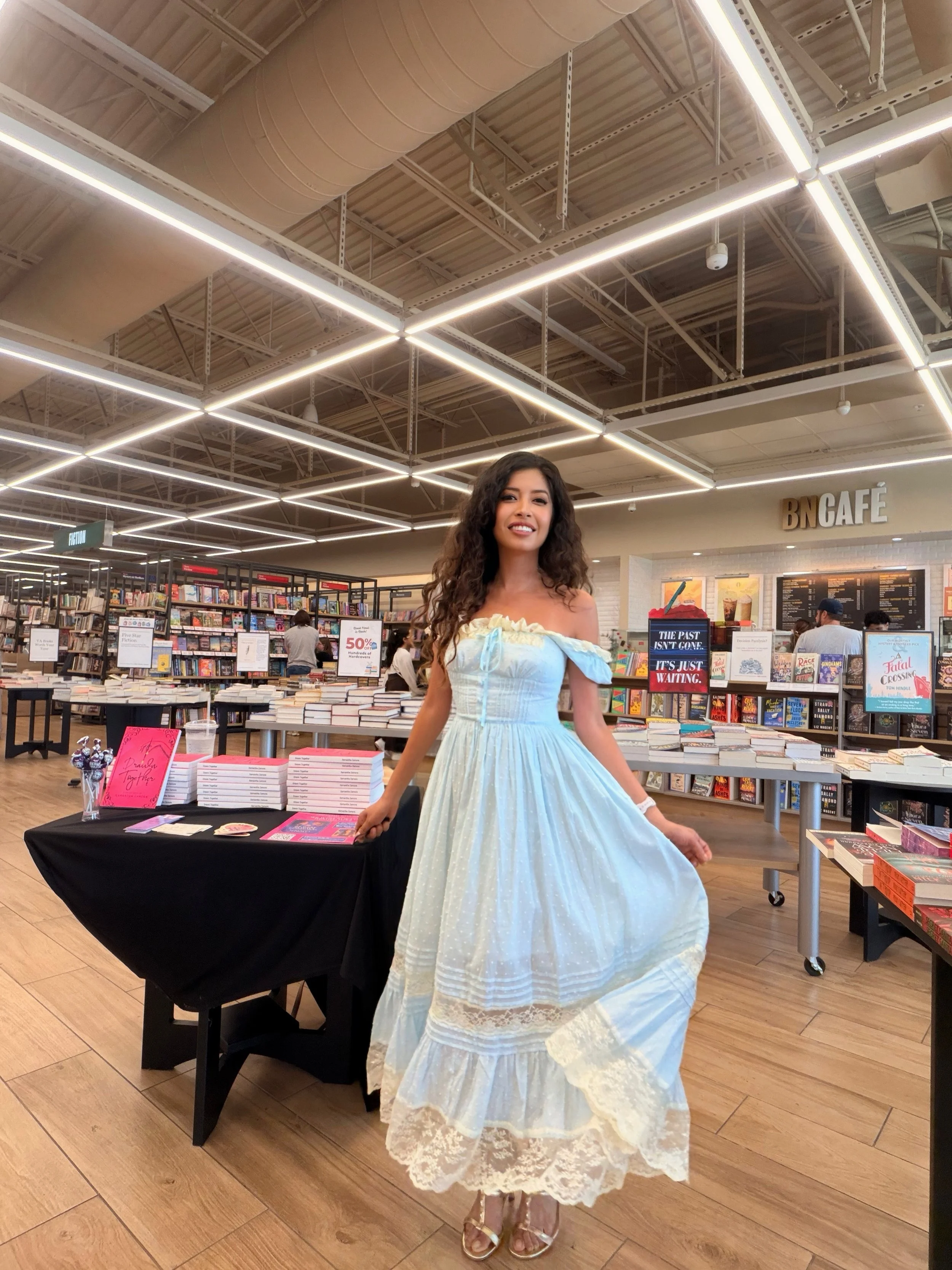 Author Samantha Zamora wearing her blue Lacemade dress beside her book signing display at Barnes & Noble in Concord, California.