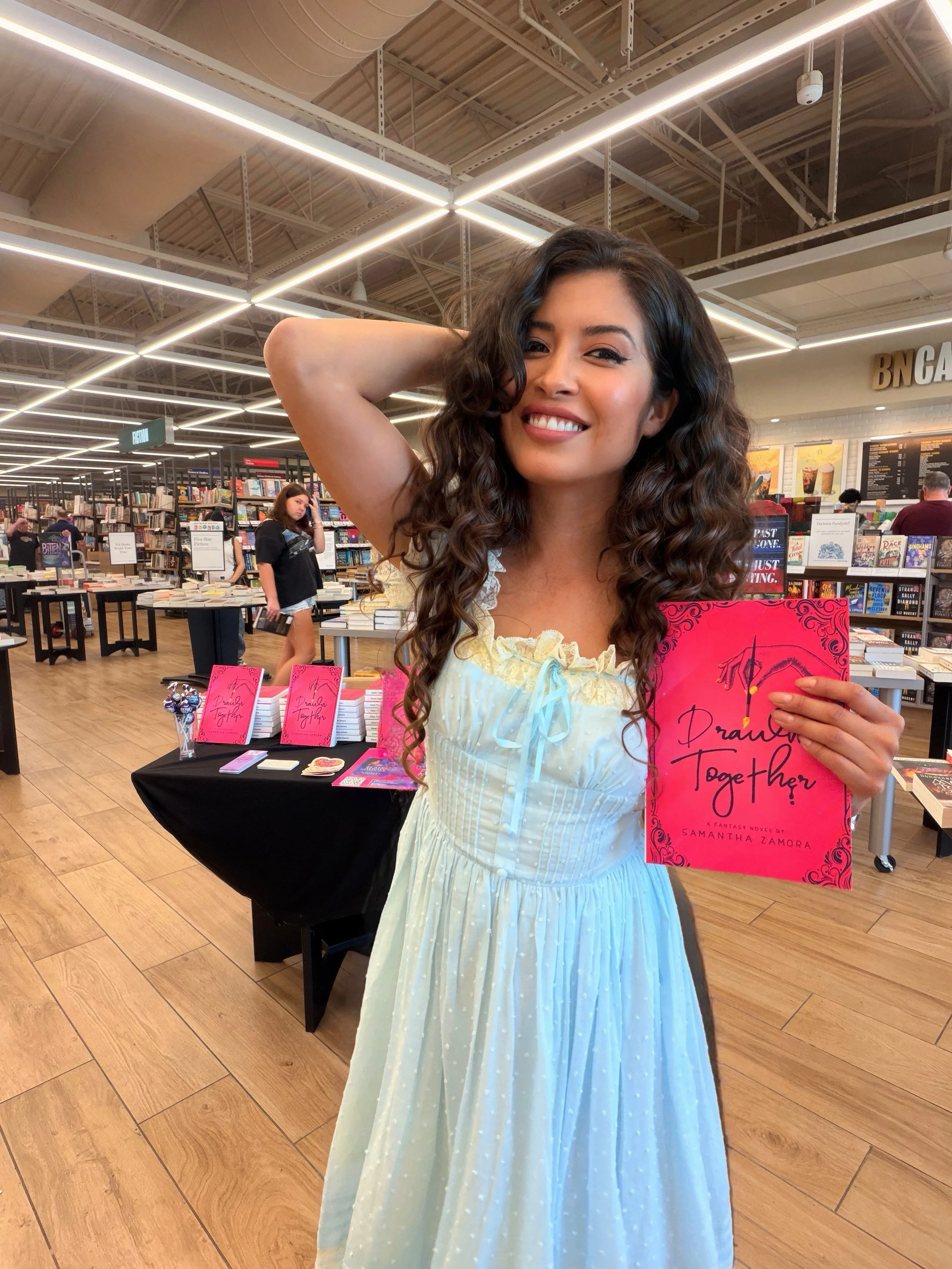 Samantha Zamora wearing a Lacemade dress and holding her novel Drawn Together at Barnes & Noble in Concord, California.