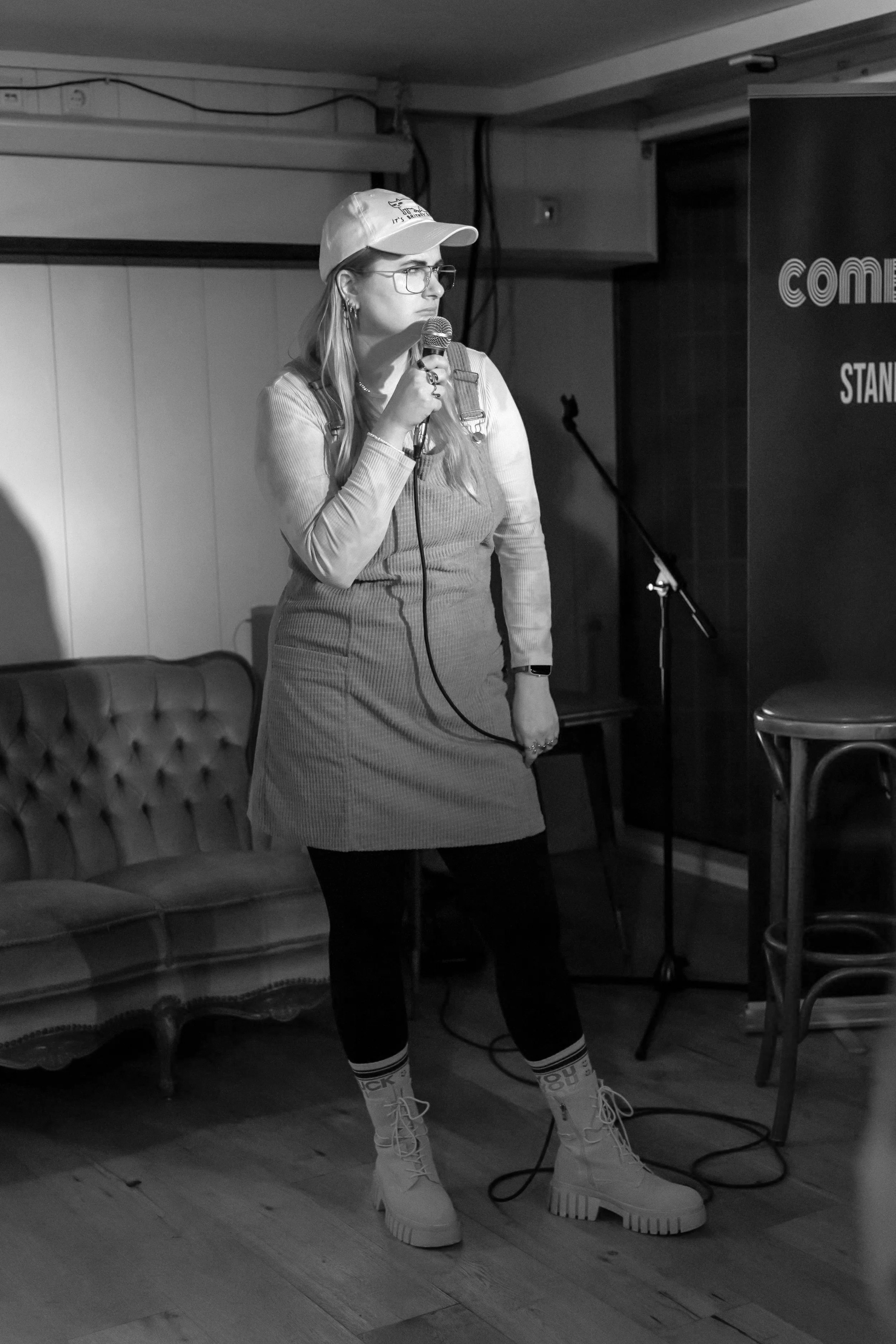 Alina trägt auf der Bühne ein Latzkleid, eine Cappy und Stiefel mit bunten Socken, sie runzelt die Stirn und schaut verdutzt drein