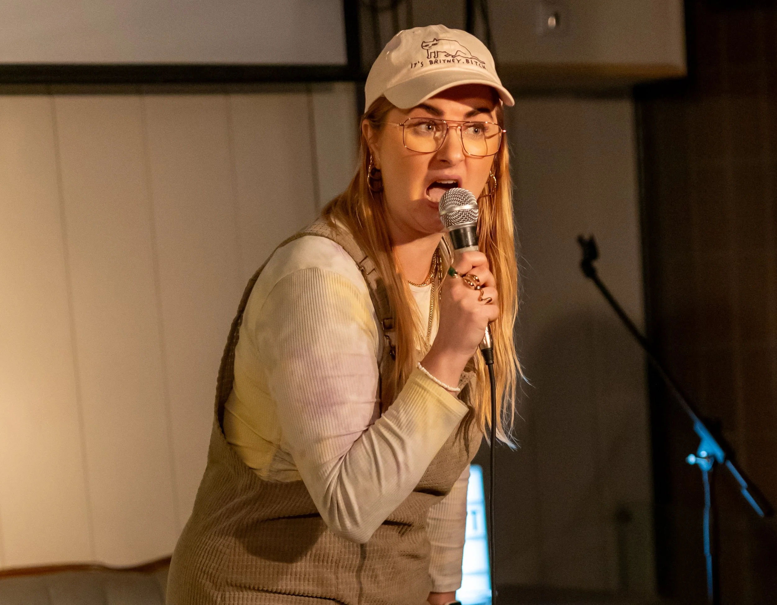 Alina trägt eine rosa cap auf der "it's britney B*tch" steht, mit aufgerissenem Mund und Augen hält sie das Mikrofon und schaut ins Publikum als würde sie gerade jemanden ausschimpfen