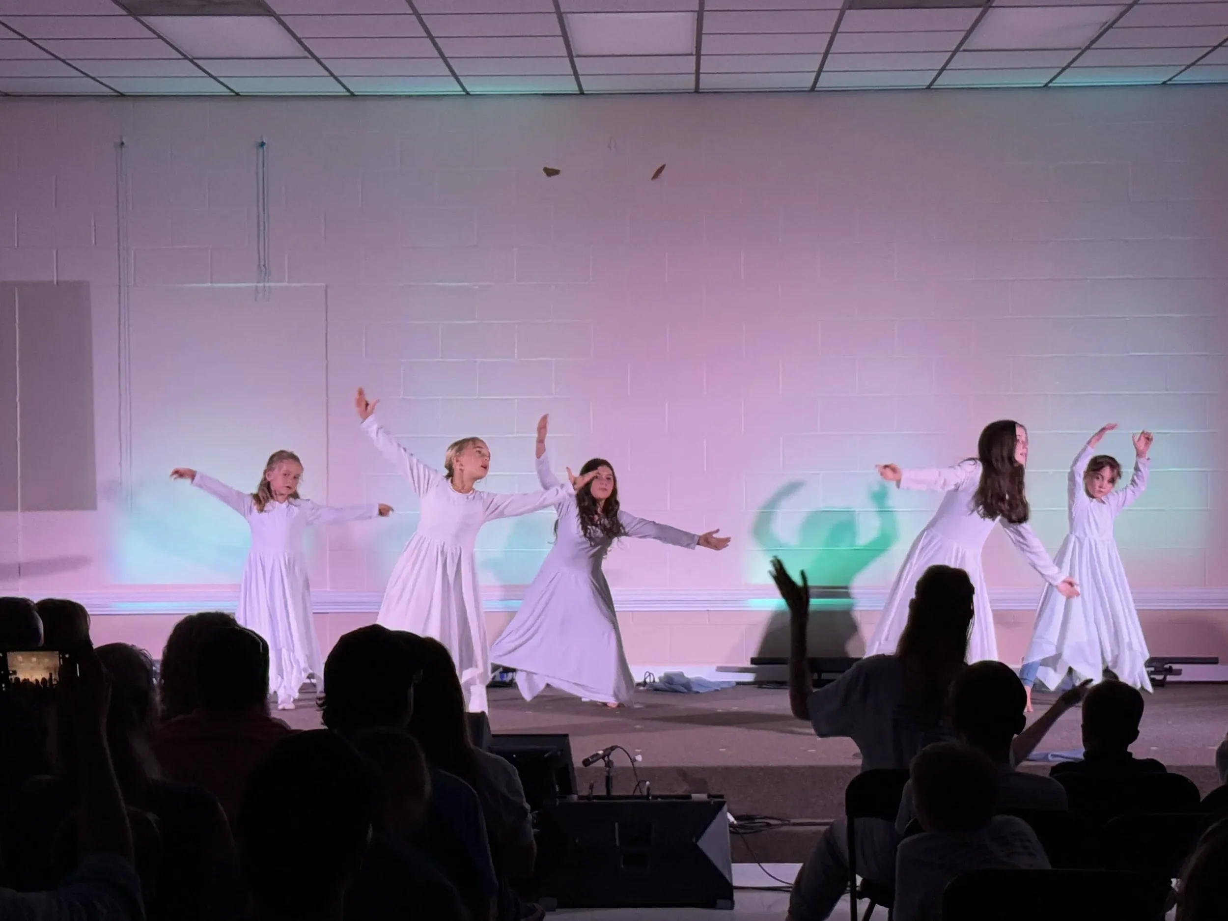  A group of dancers perform a worship dance on stage under soft pink and green lighting. 