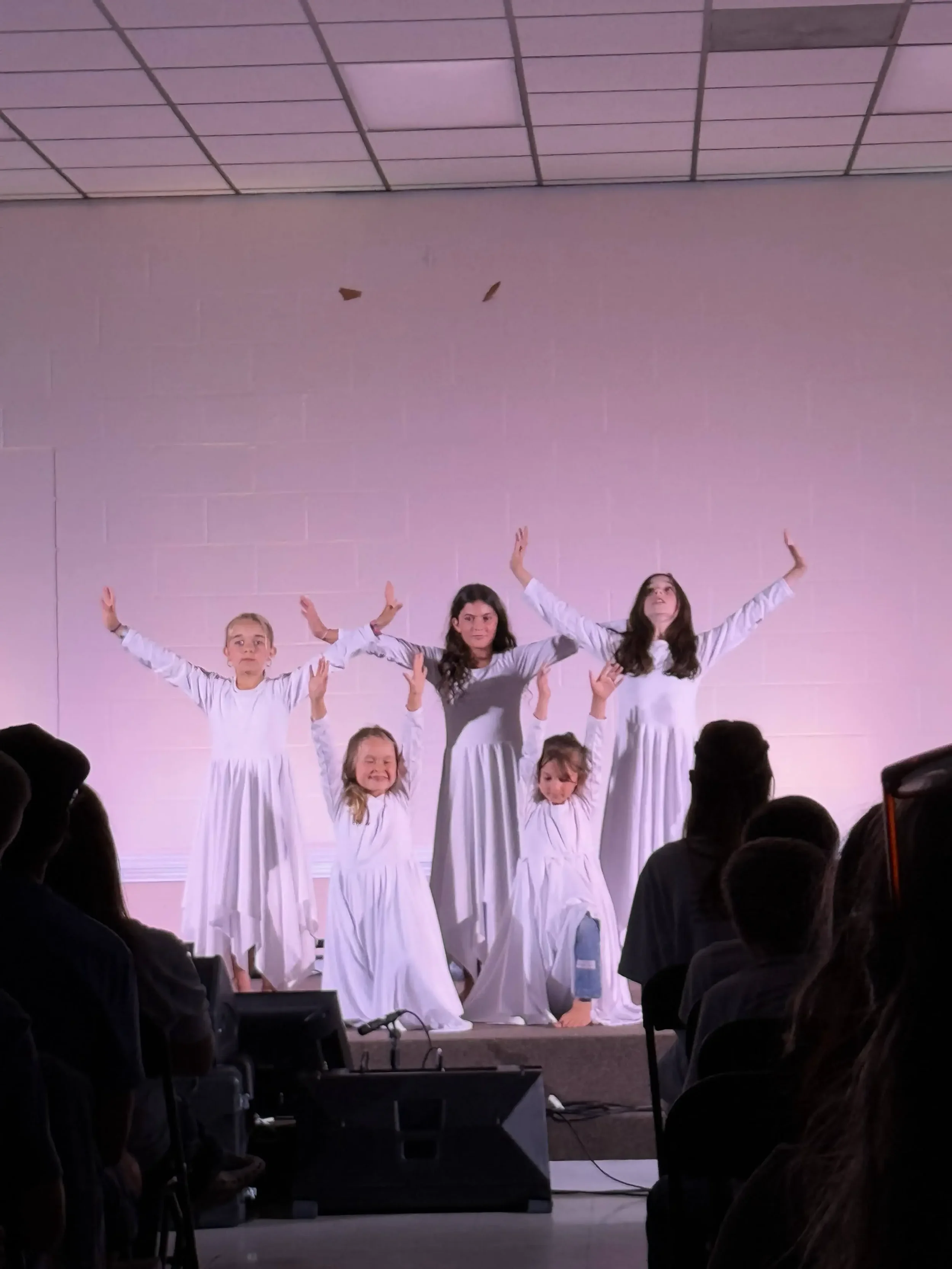  Five dancers in white dresses hold a final worship pose on stage as the audience watches. 