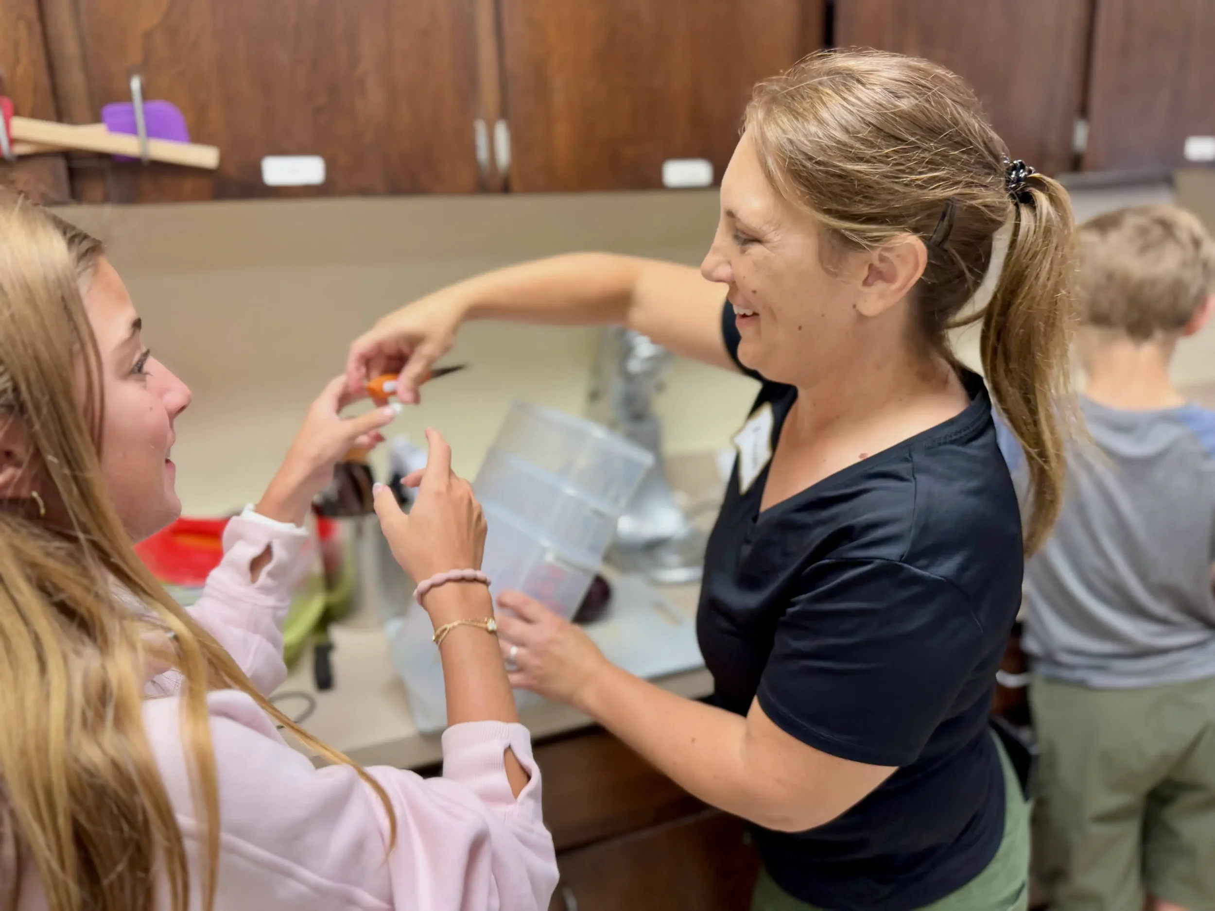  An instructor smiles while handing a small ingredient to a child during a cooking activity. 
