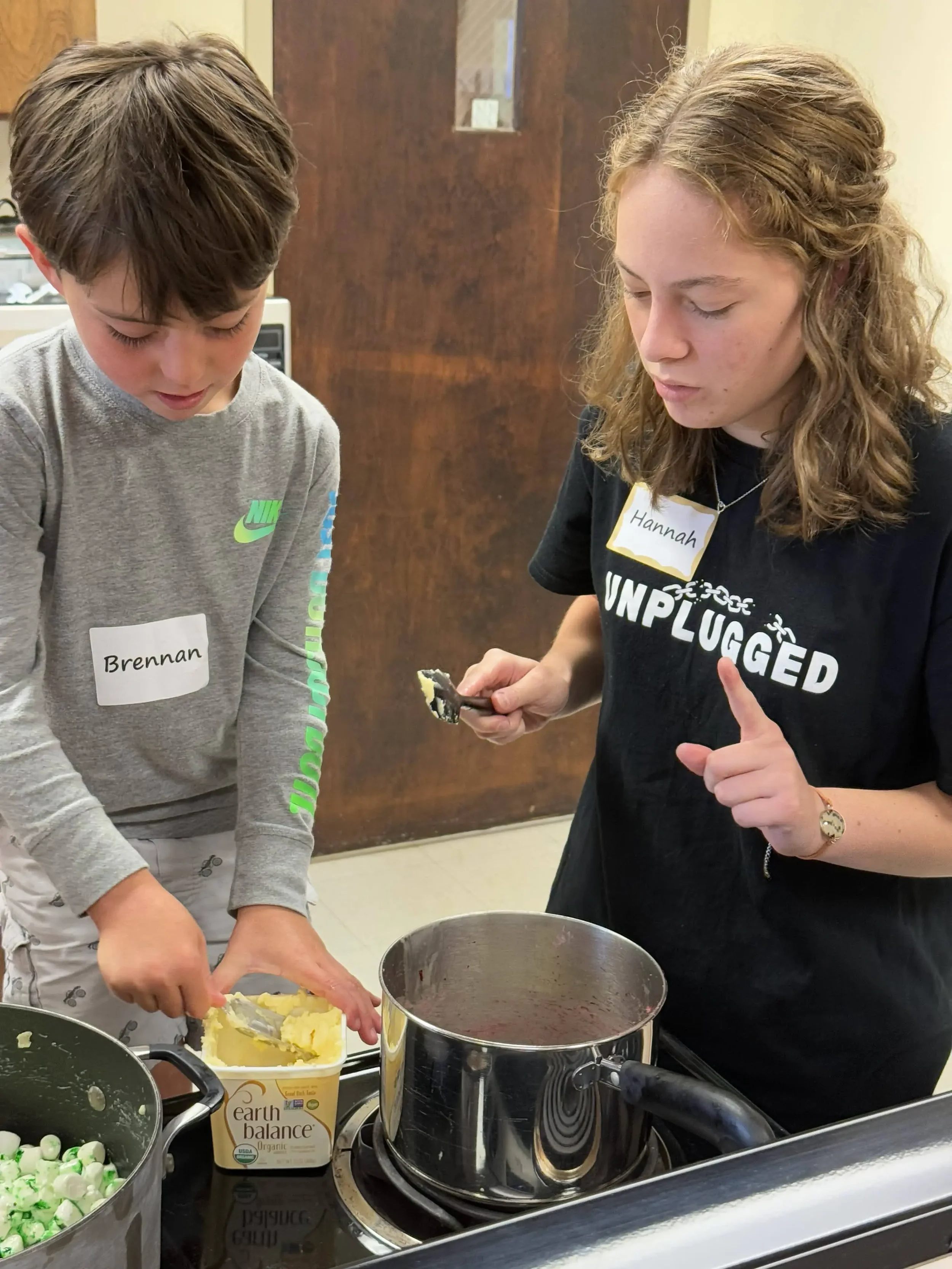 A teen instructor guides a child while measuring dairy-free butter for a cooking project.