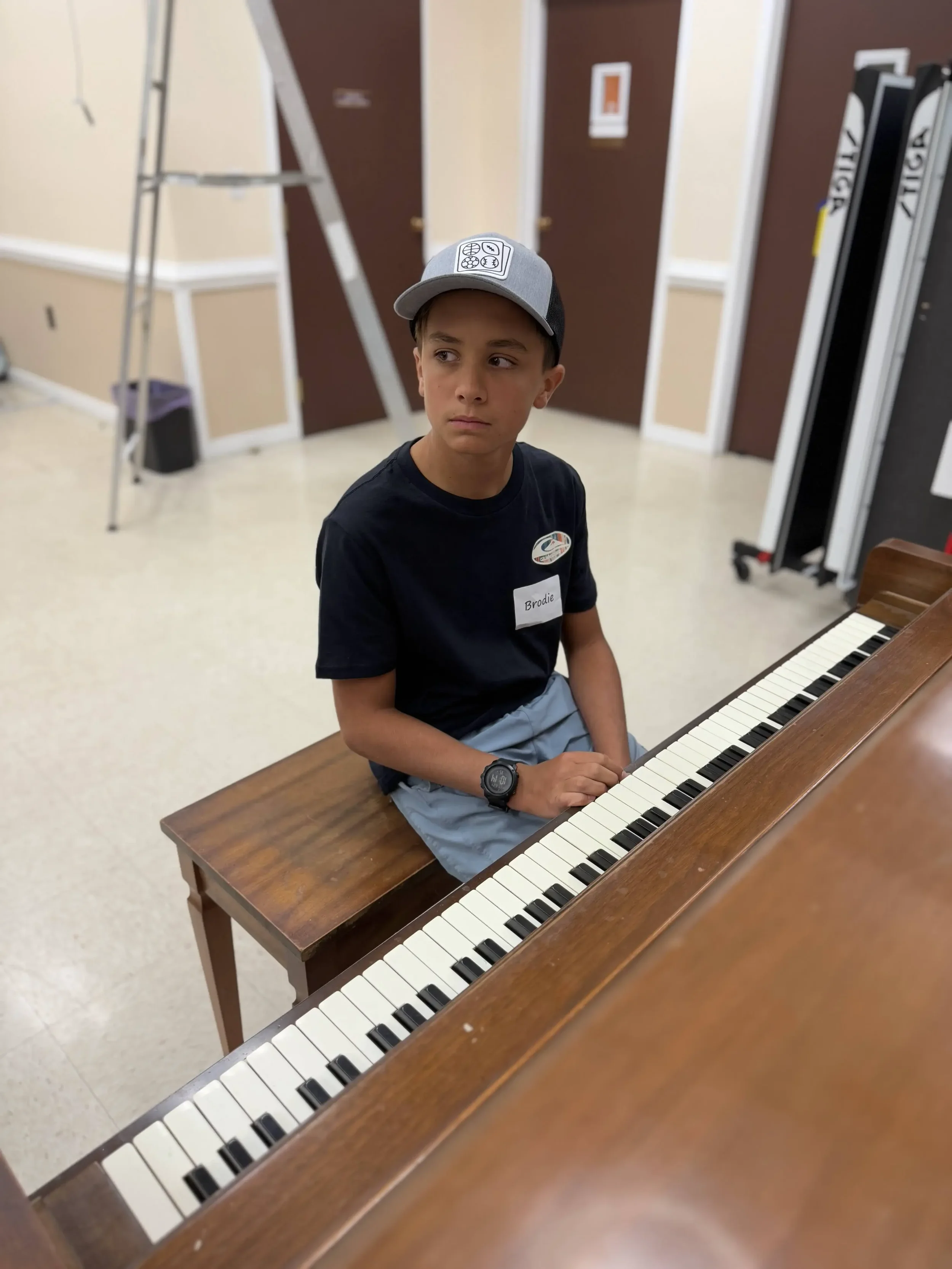 A boy sits at a piano bench, listening attentively during a music session.