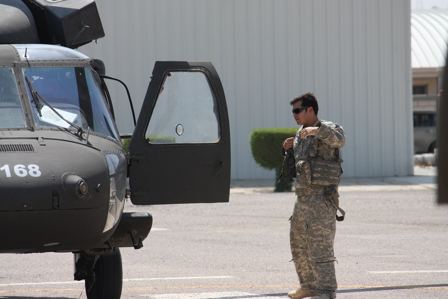 A soldier in camouflage uniform and sunglasses standing next to a military helicopter on a tarmac.