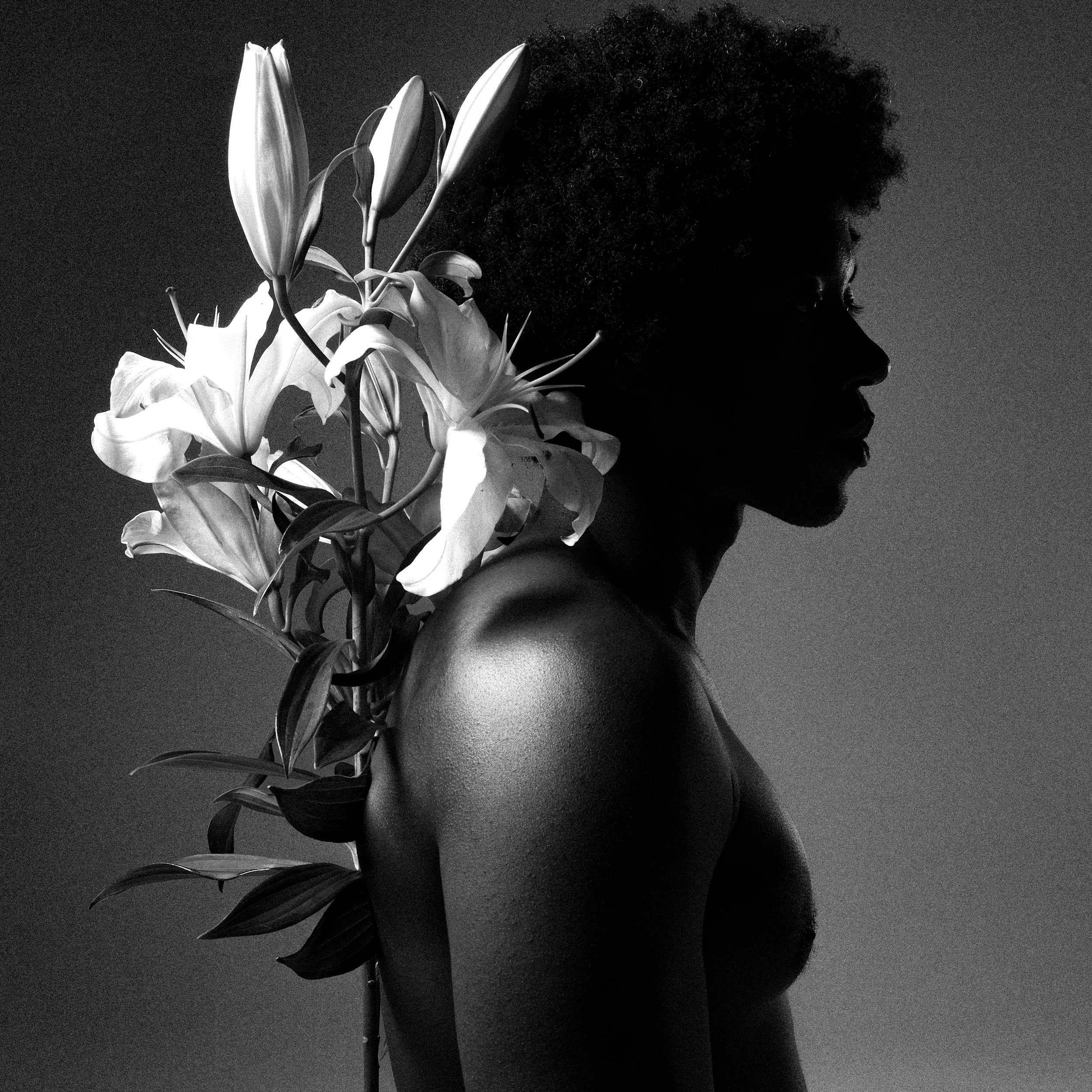 Black and white photo of a woman with an afro hairstyle, with a bouquet of lilies overlapping her face in profile view.