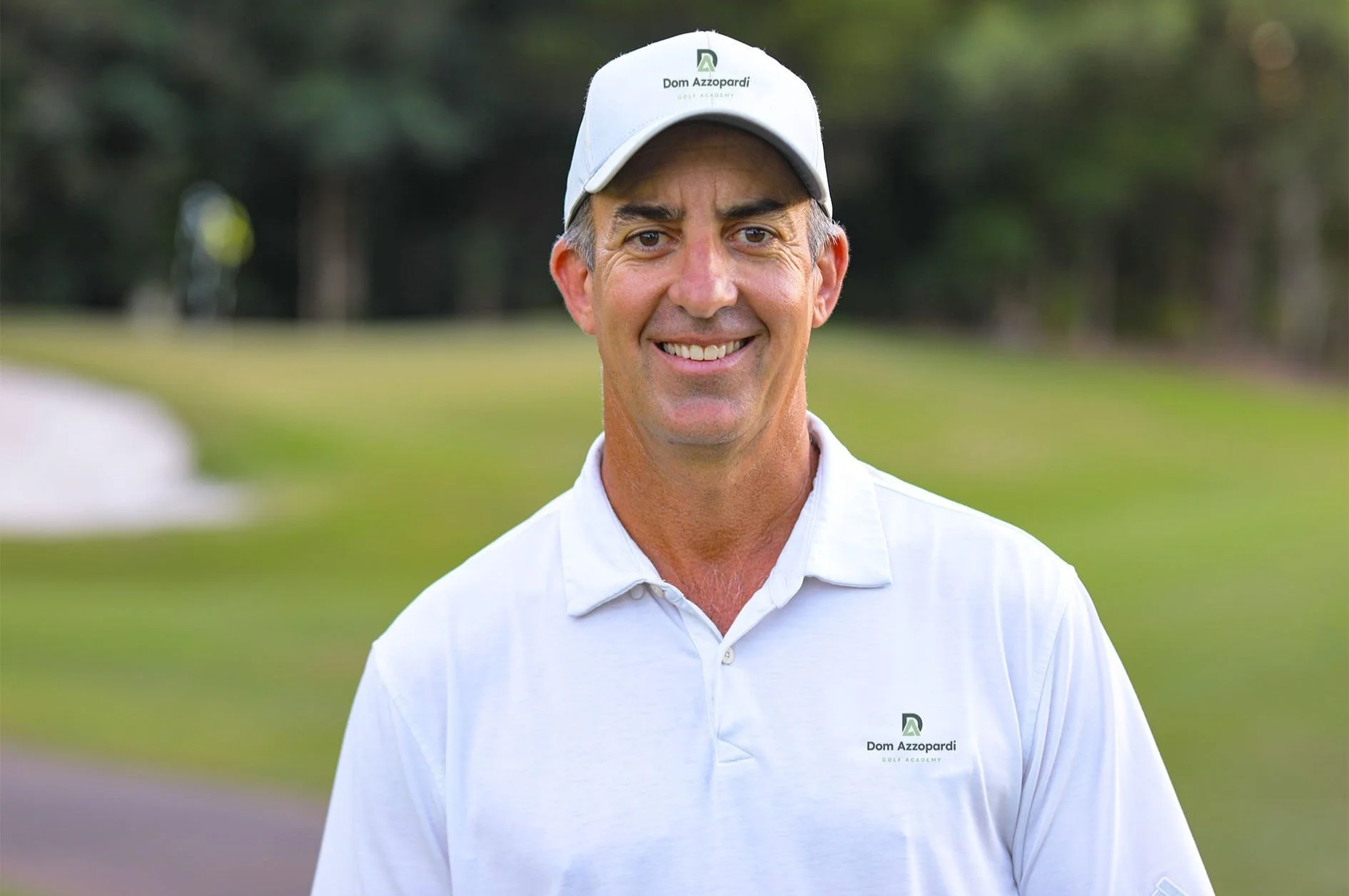 PGA Professional Dom Azzopardi, smiling, dressed in white golf shirt and cap standing on golf course