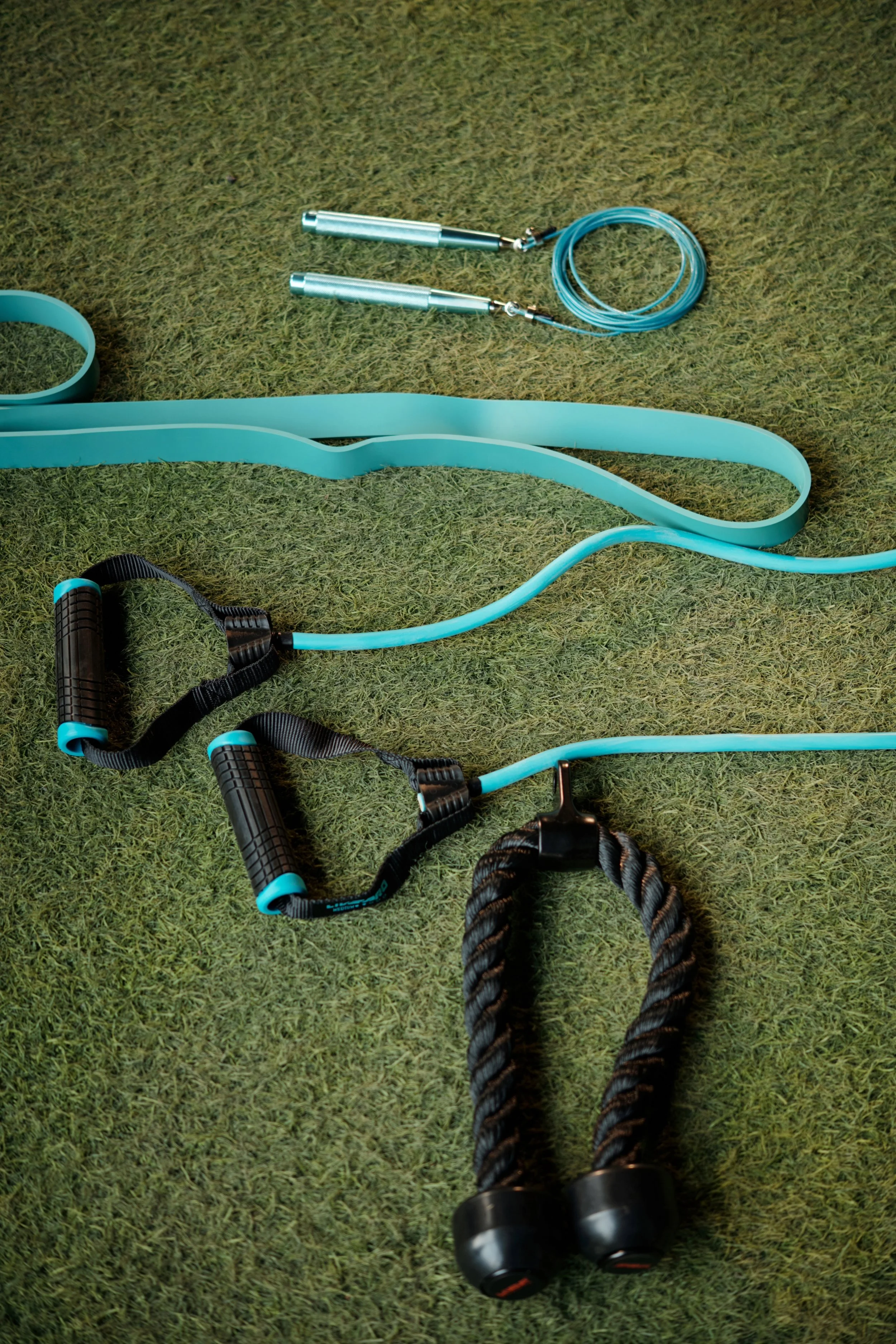 Set of fitness equipment on green gym mat, including foam resistance bands, jump rope, and hand-held weights with handles.