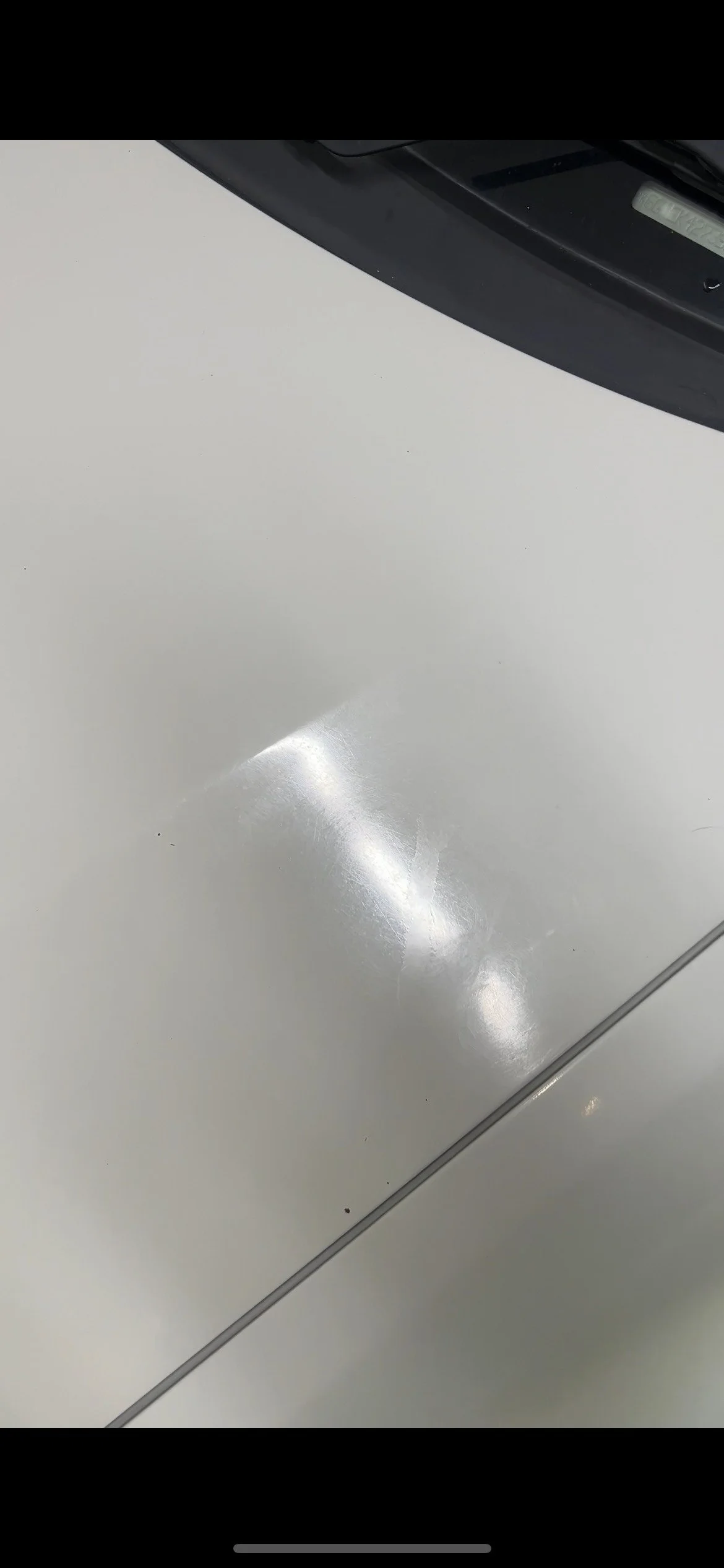 Close-up of a white car's surface with a visible dent and light reflection, with part of the black bumper at the top.