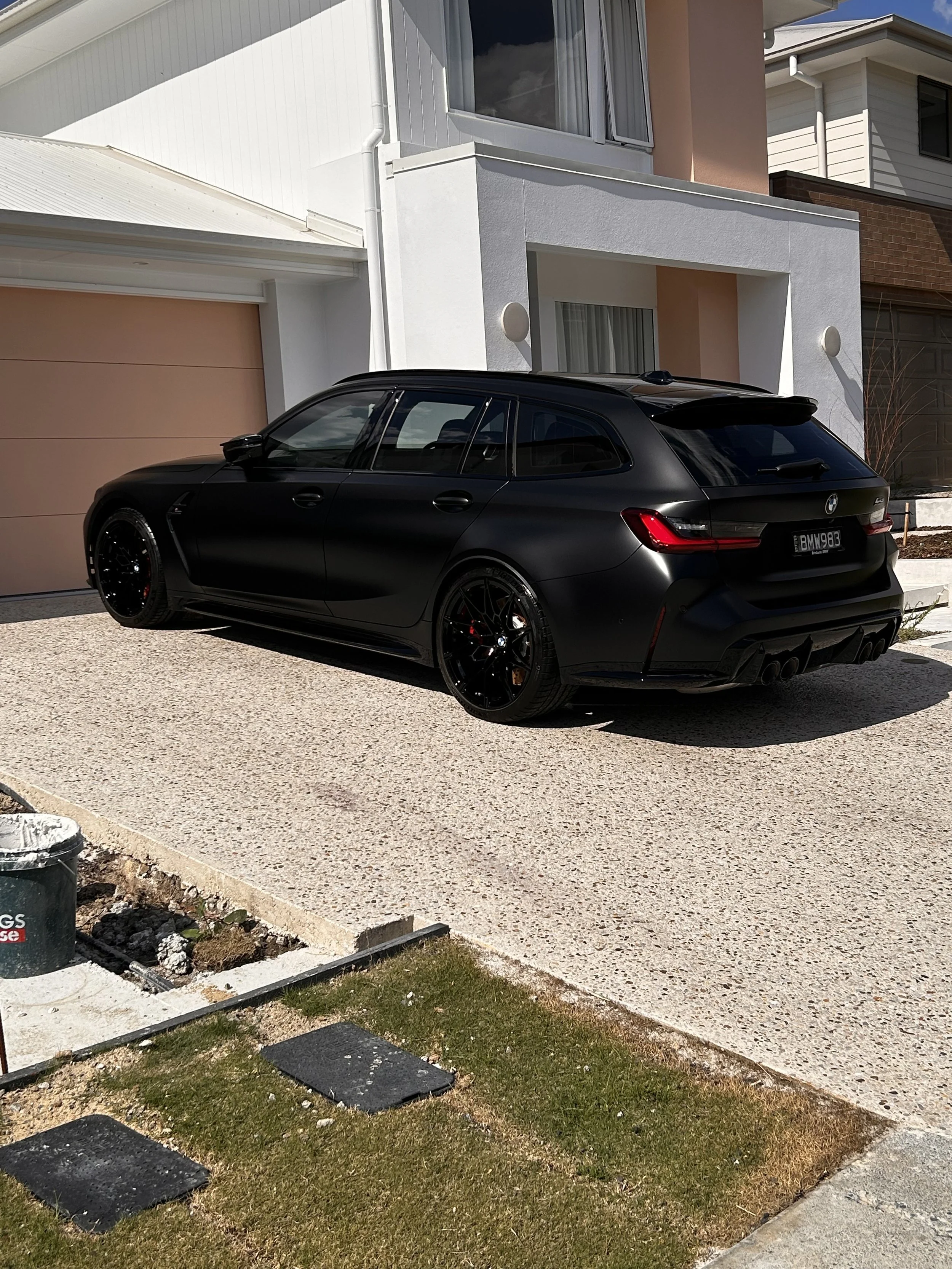 A black BMW station wagon parked in front of a modern house with white and peach exterior walls and a brown garage door.