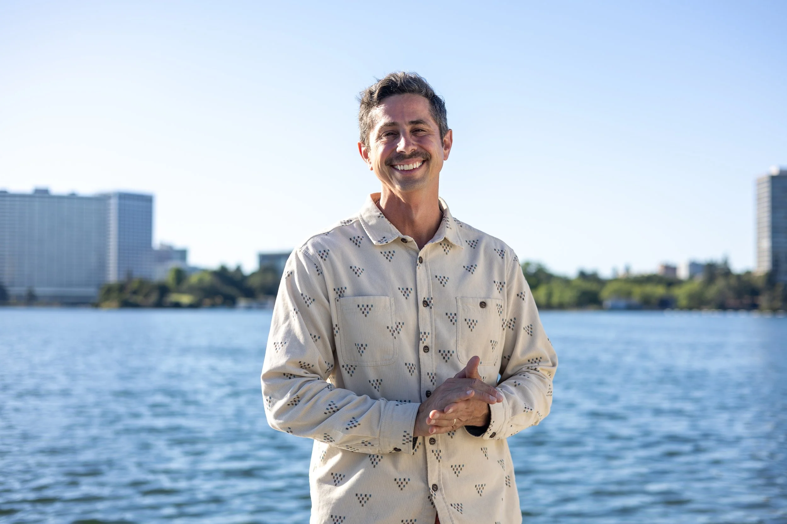 Eli smiling in front of Lake Merritt with downtown Oakland in the background.