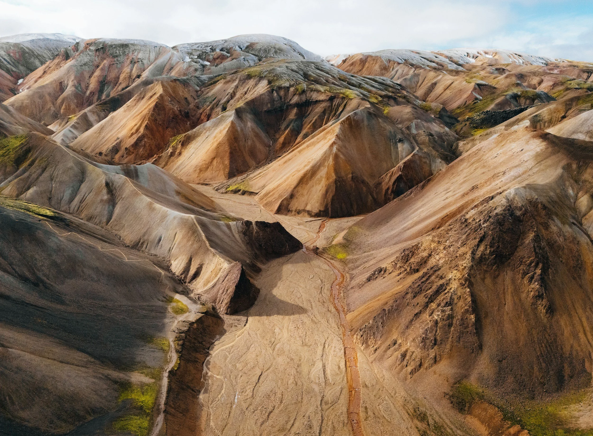 Aerial view of colorful rhyolite mountains in Landmannalaugar, Iceland, with winding river and barren landscape.