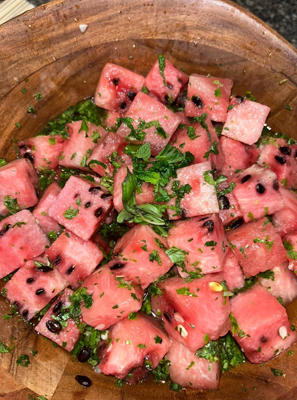 Diced watermelon with chopped mint and cilantro, garnished with black seeds, served in a wooden bowl.