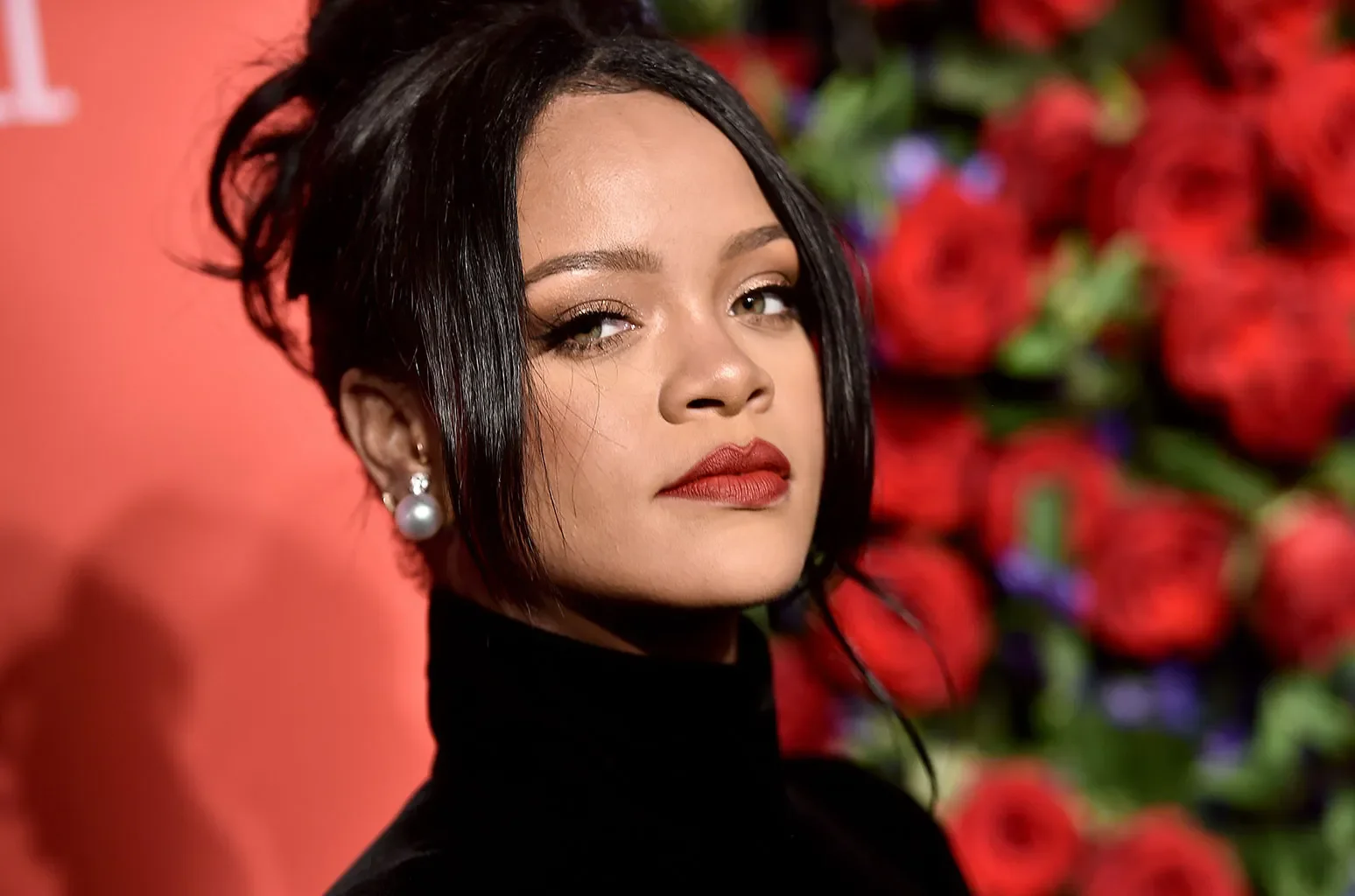 Rihanna in a black pullover against a red backdrop with flowers