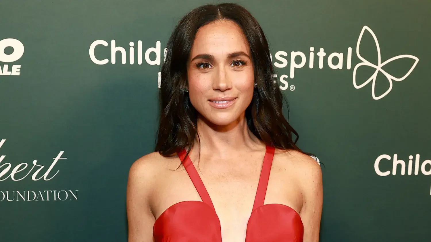Meghan Markle in a red strap dress against a green background
