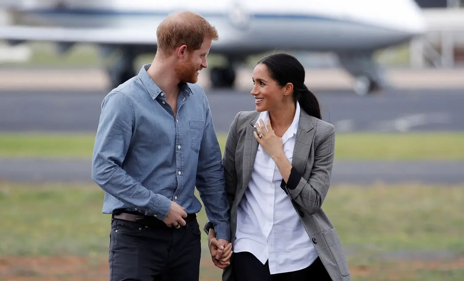 Harry and Meghan with a plane in the background, looking at each other lovingly