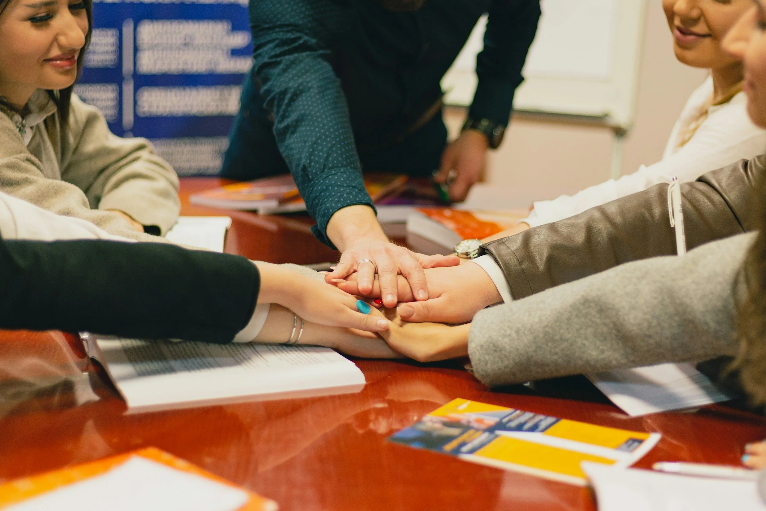 Group of people with different colored sweaters joining hands in a circle, symbolizing unity.