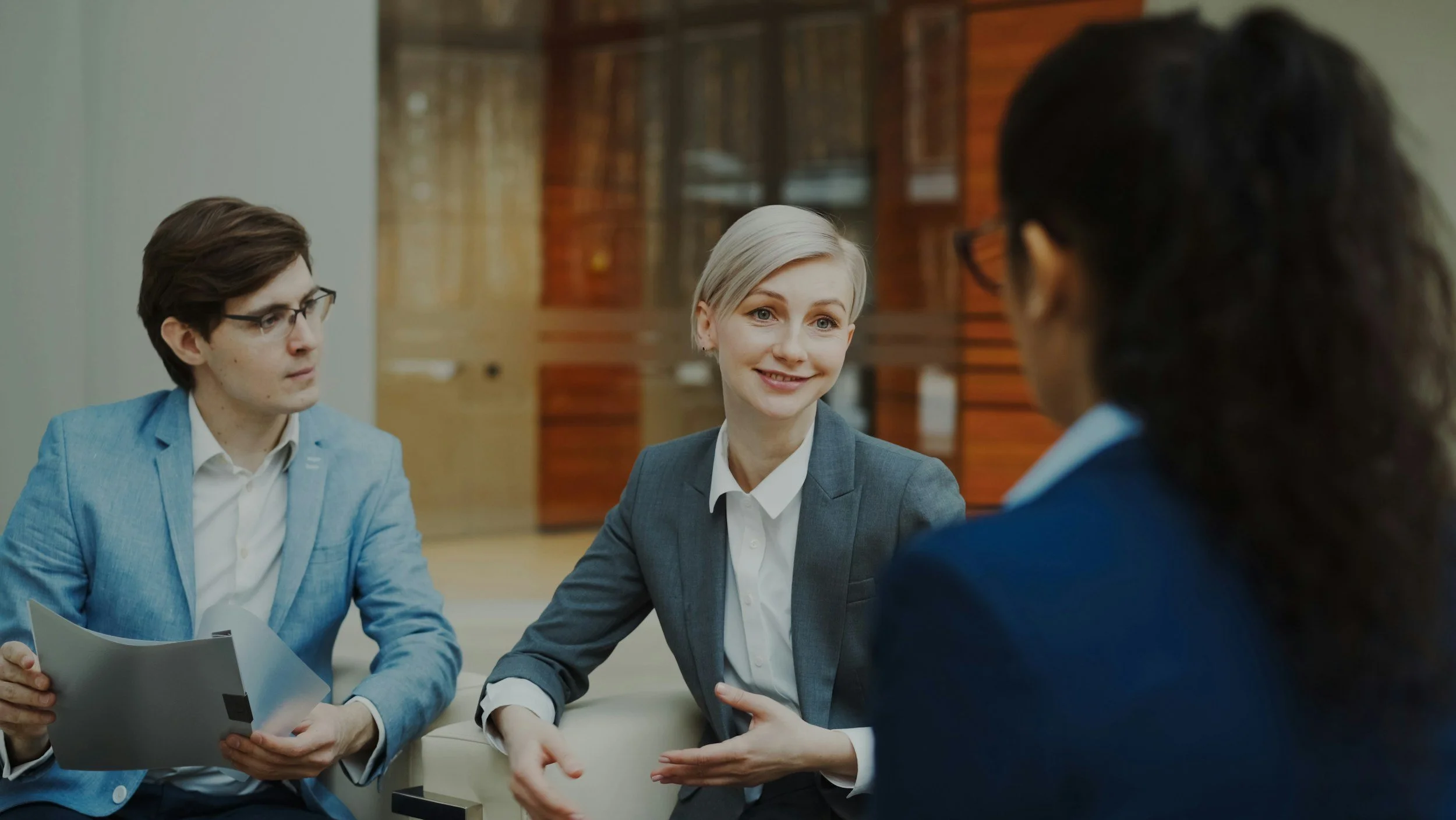 Group of people in a meeting with notebooks and pens on a wooden table.