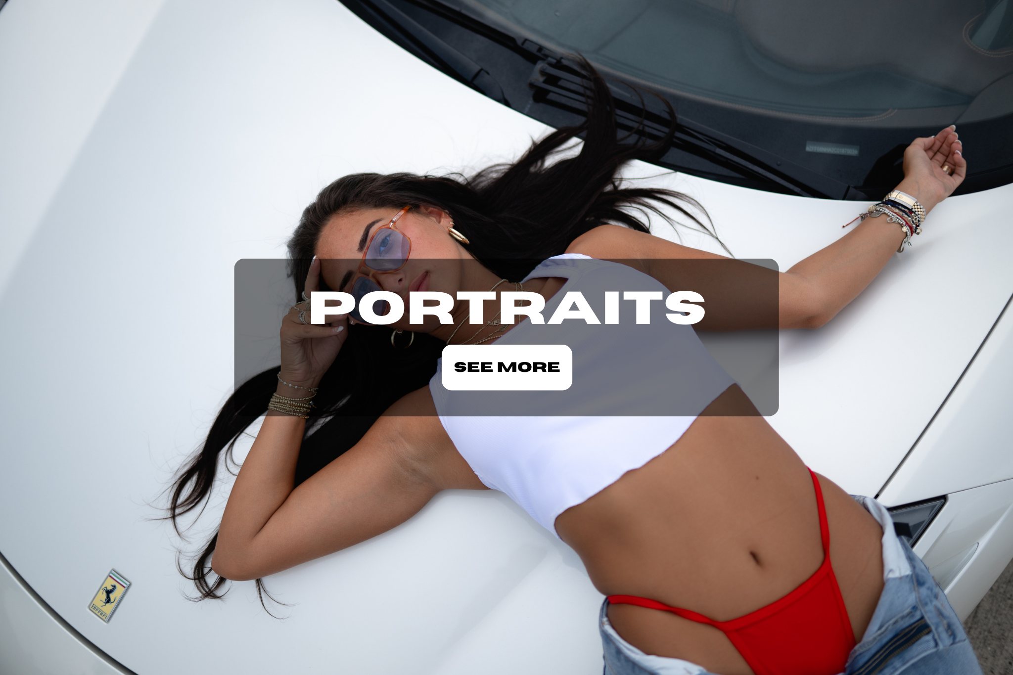 A woman with long dark hair wearing sunglasses, a white crop top, red bikini bottoms, and denim shorts, lying on a white car with a Ferrari logo, in a relaxed pose.