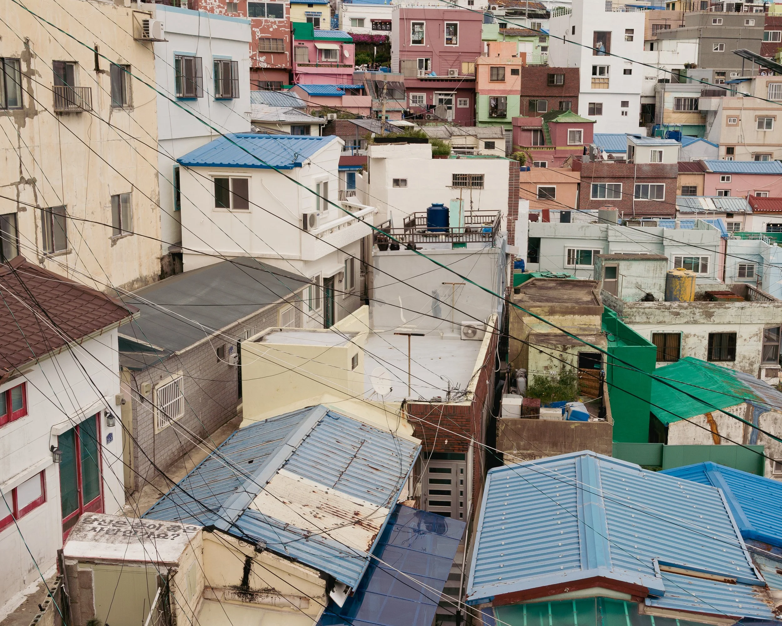 A densely packed urban neighborhood with colorful buildings and rooftops, seen from above, with electrical wires crossing the scene.