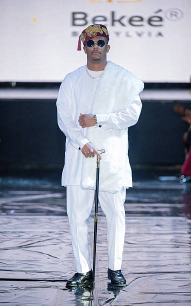 A man wearing sunglasses, a crown, and an all-white outfit holding a cane on a stage.