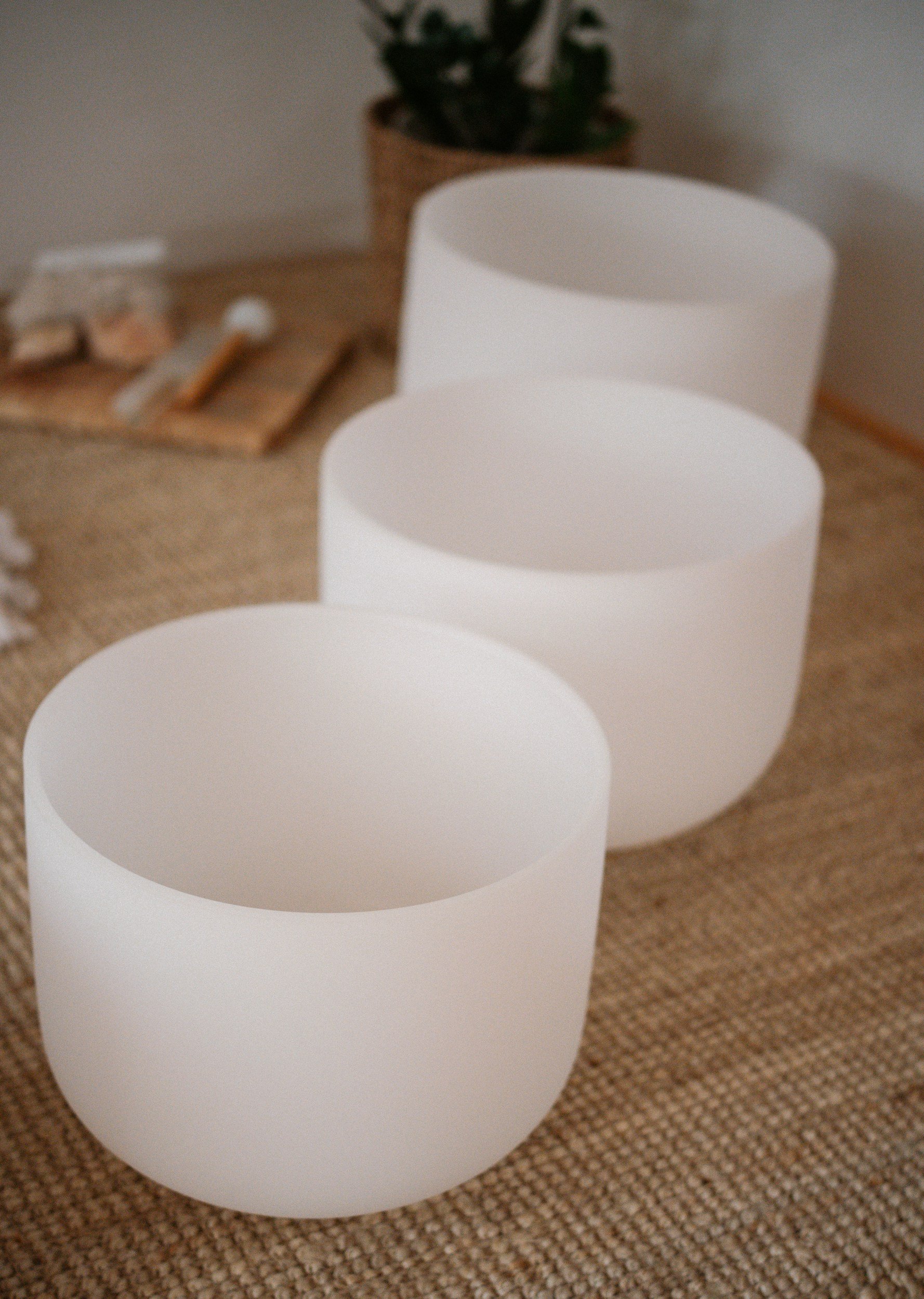 A row of three white lanterns on a beige carpet, with a potted plant and some miscellaneous items blurred in the background.