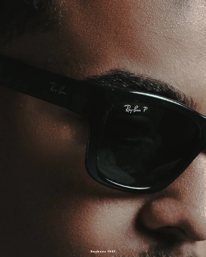 Close-up image of a person wearing black Ray-Ban sunglasses, showing part of their nose and cheek with smooth skin.