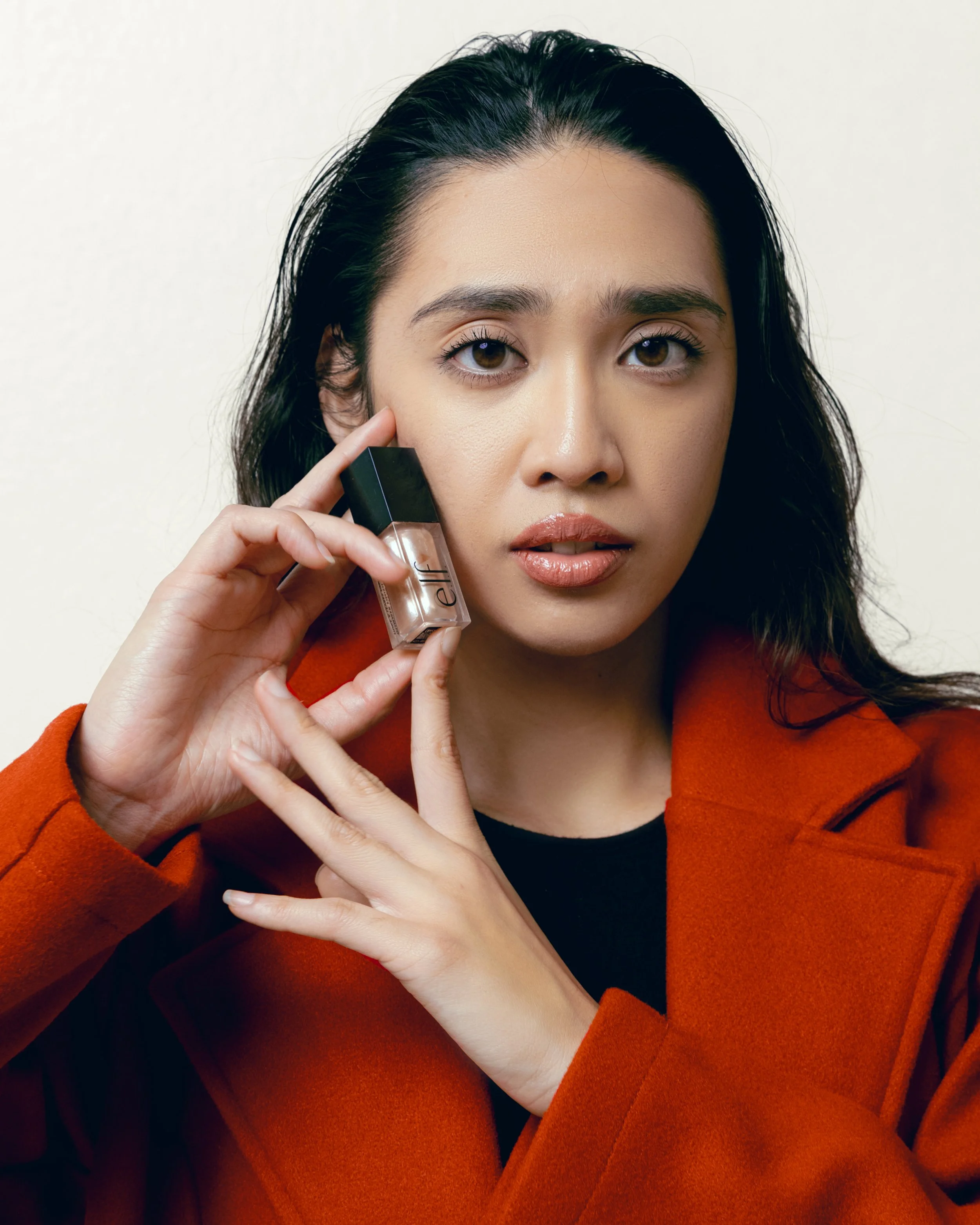 Woman holding a bottle of nail polish while looking at the camera.