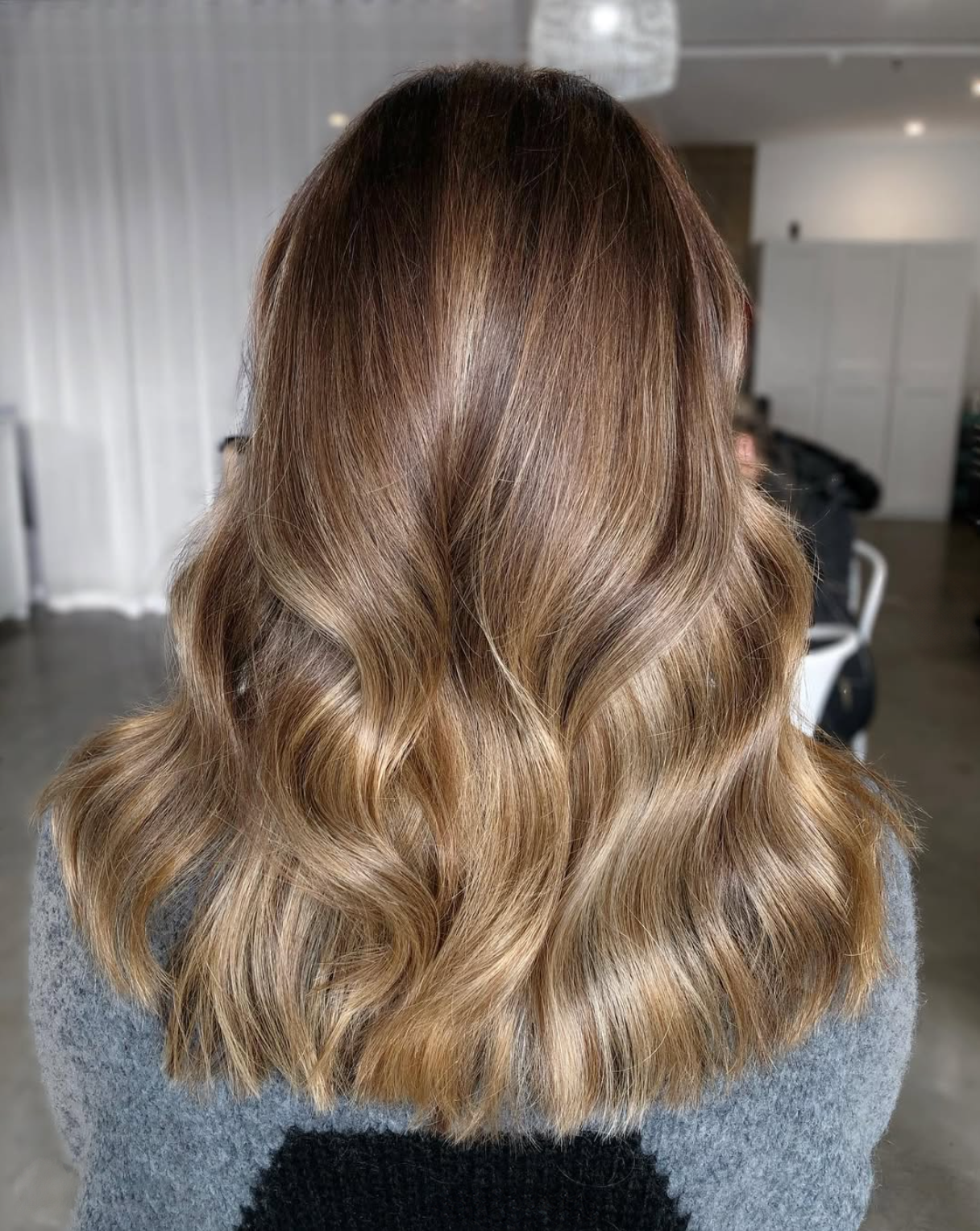 Back view of a woman with long, wavy, ombre hair that transitions from dark brown at the roots to light blonde at the ends.