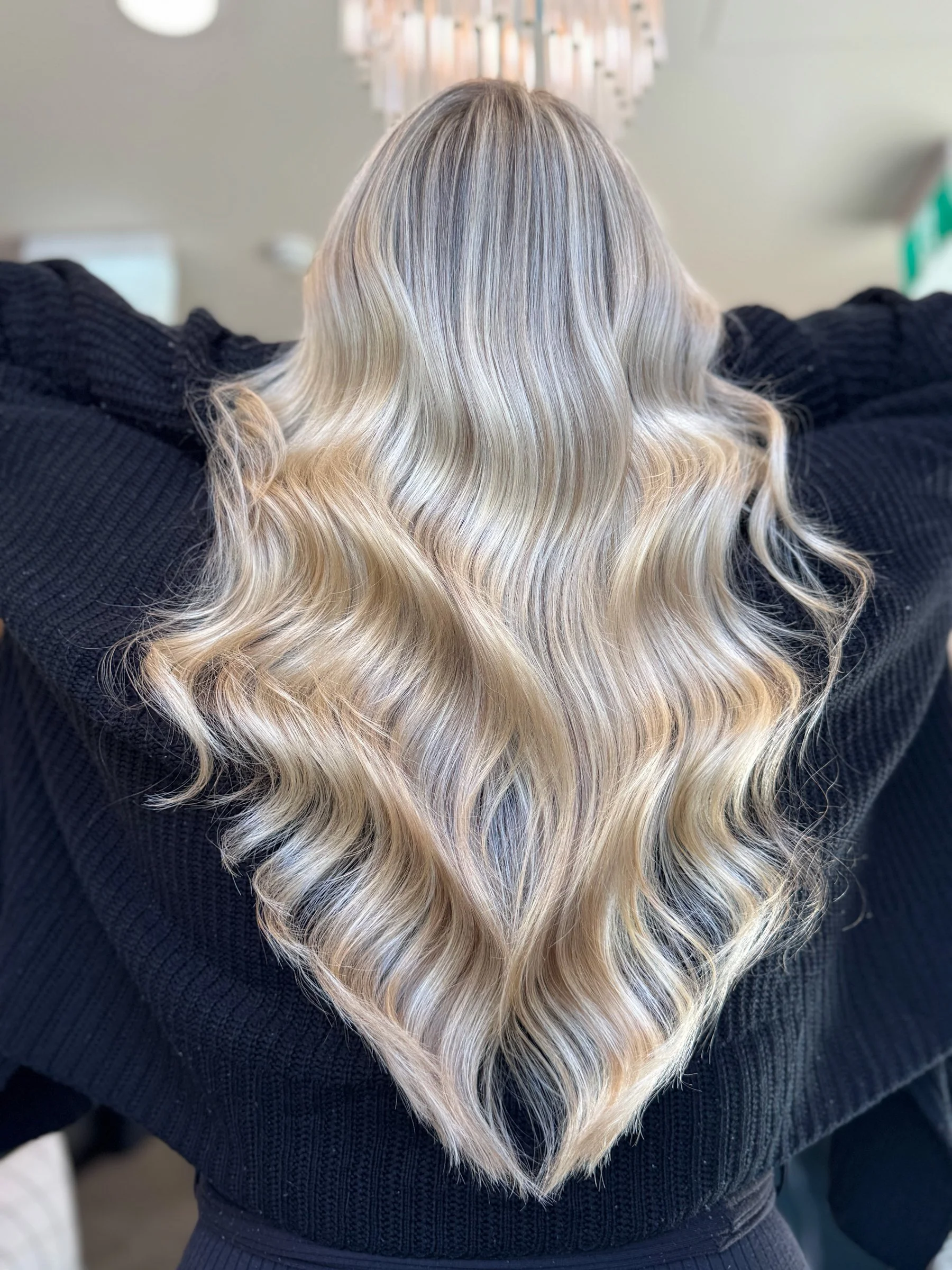 Back view of a woman with long, wavy blonde hair wearing a black sweater.