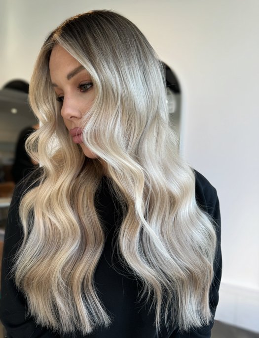 A woman with long, wavy blonde hair looking down, wearing a black top.
