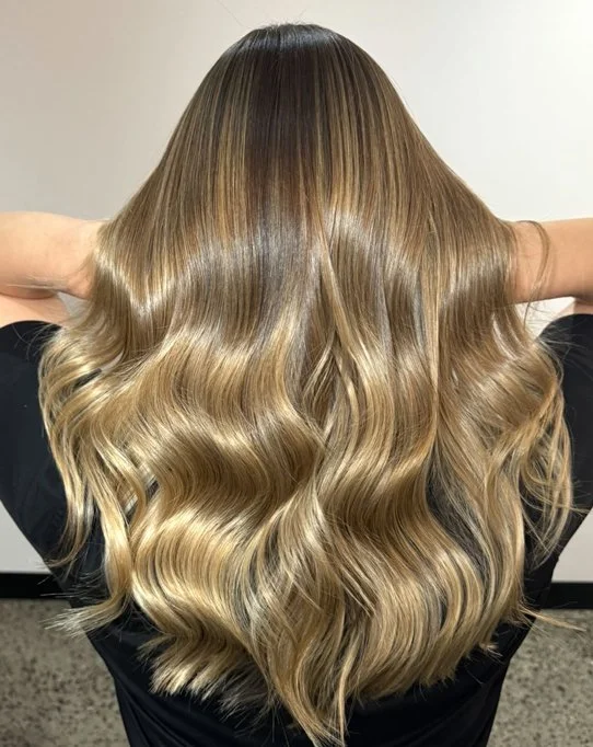 Back view of a woman with long, wavy, blonde hair, holding her hair back.