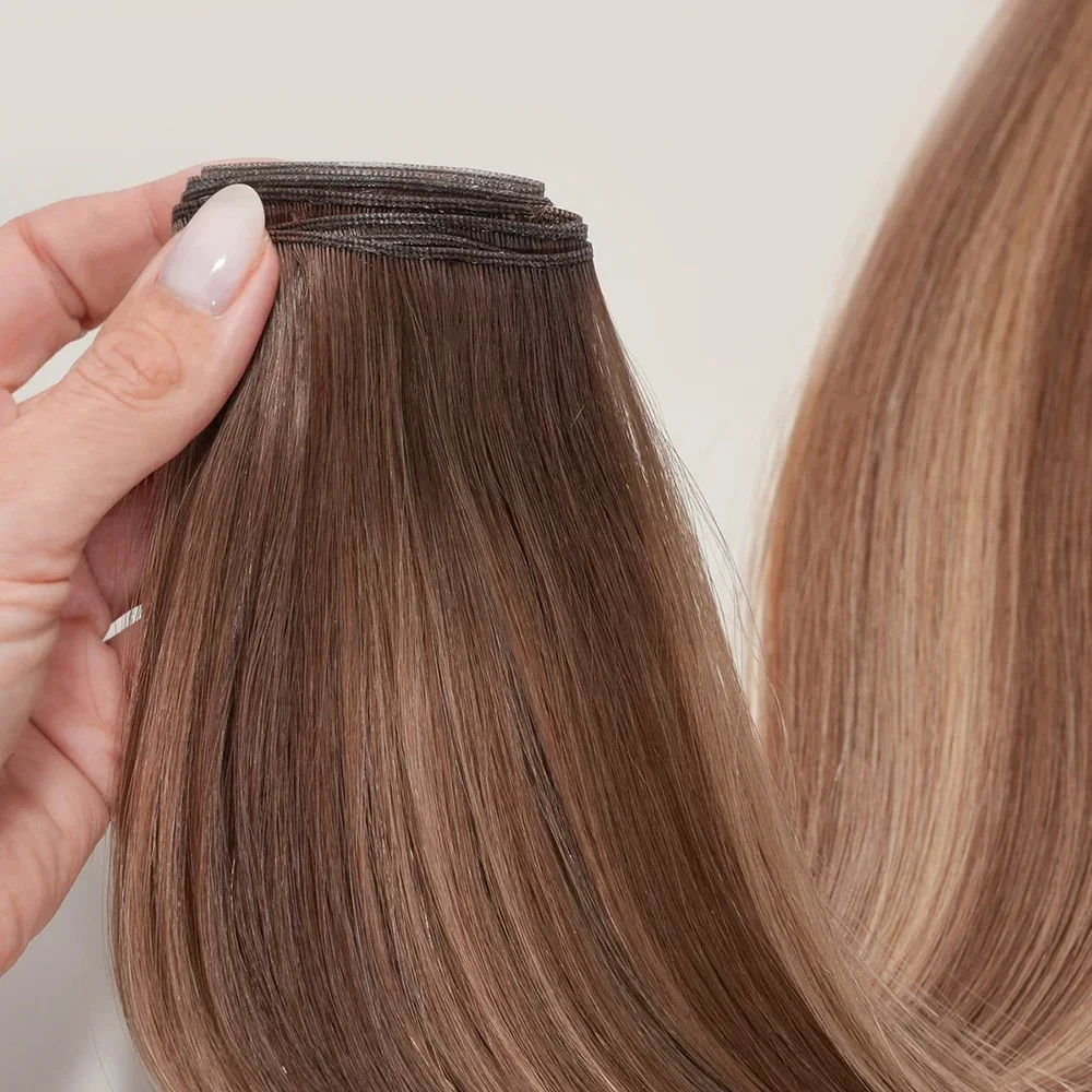 A person holding a clip-in hair extension with light brown, straight, shiny hair next to a mannequin or another hair extension of the same color.