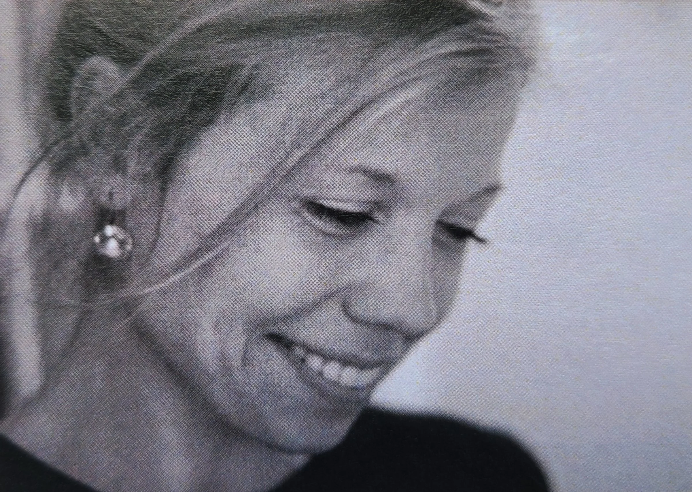 Close-up black and white photograph of a woman smiling gently with her eyes closed, wearing a pearl earring.