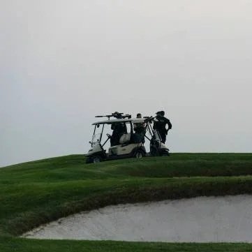 A golf cart on a grassy hilltop with a person standing next to it, under a cloudy sky.