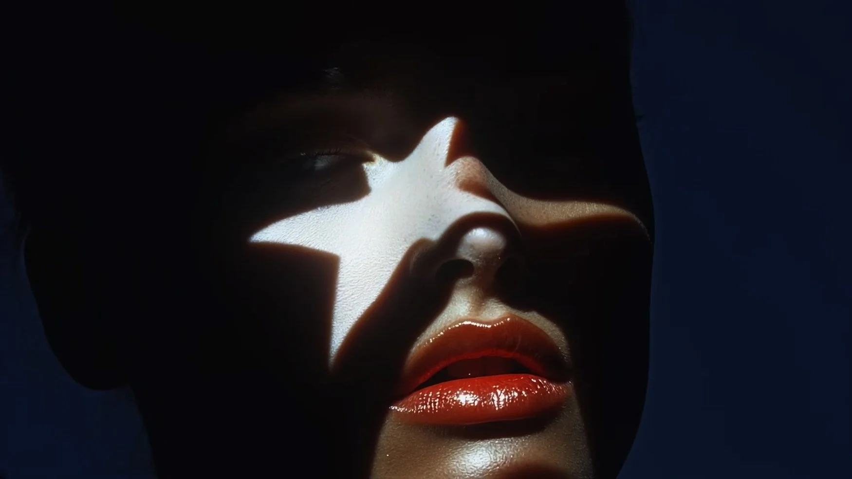 Close-up of a person's face with dramatic lighting casting shadows, highlighting their nose and lips with glossy lipstick.