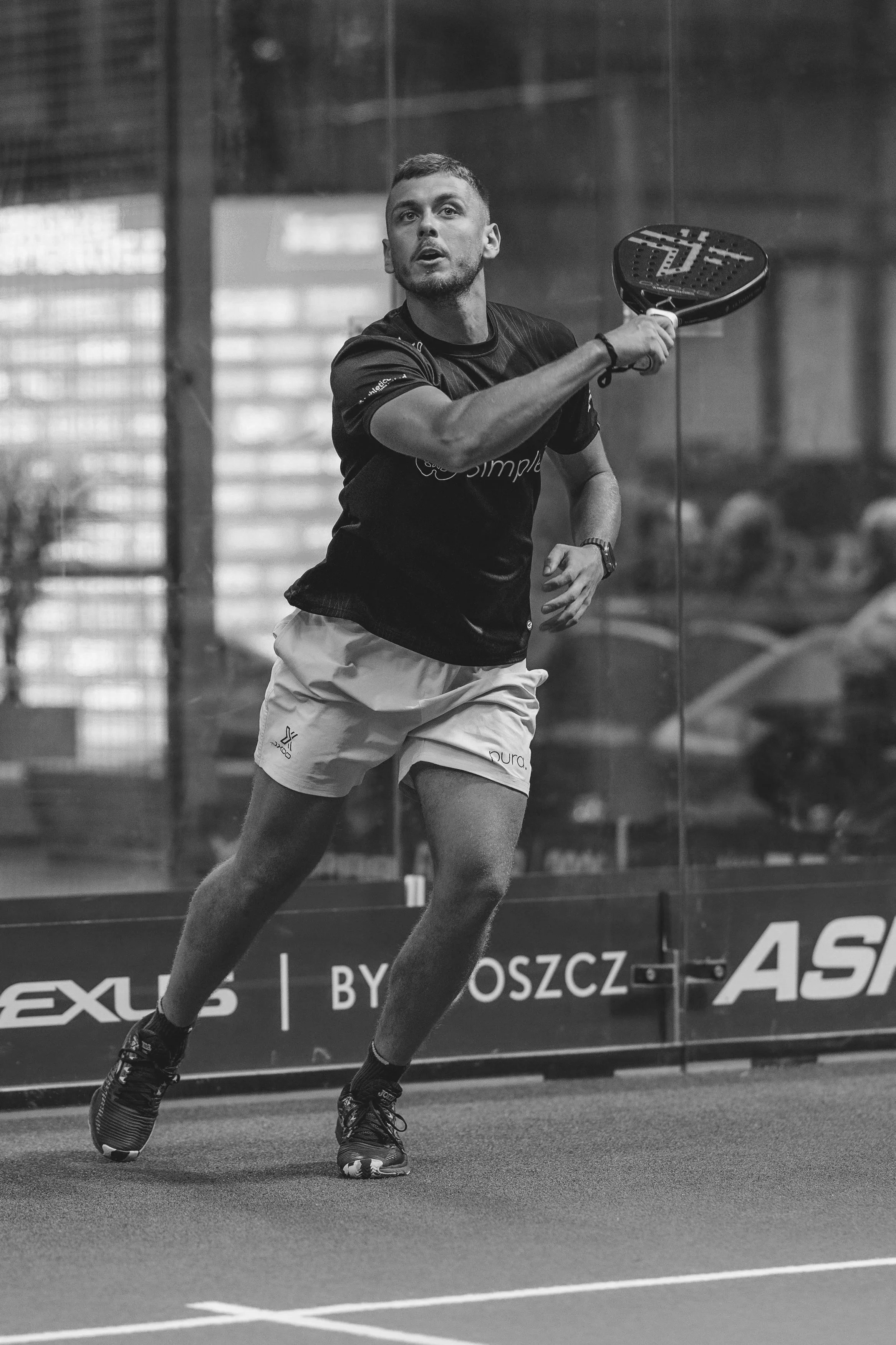 A male tennis player in action on an indoor court, preparing to hit a ball with a racket.