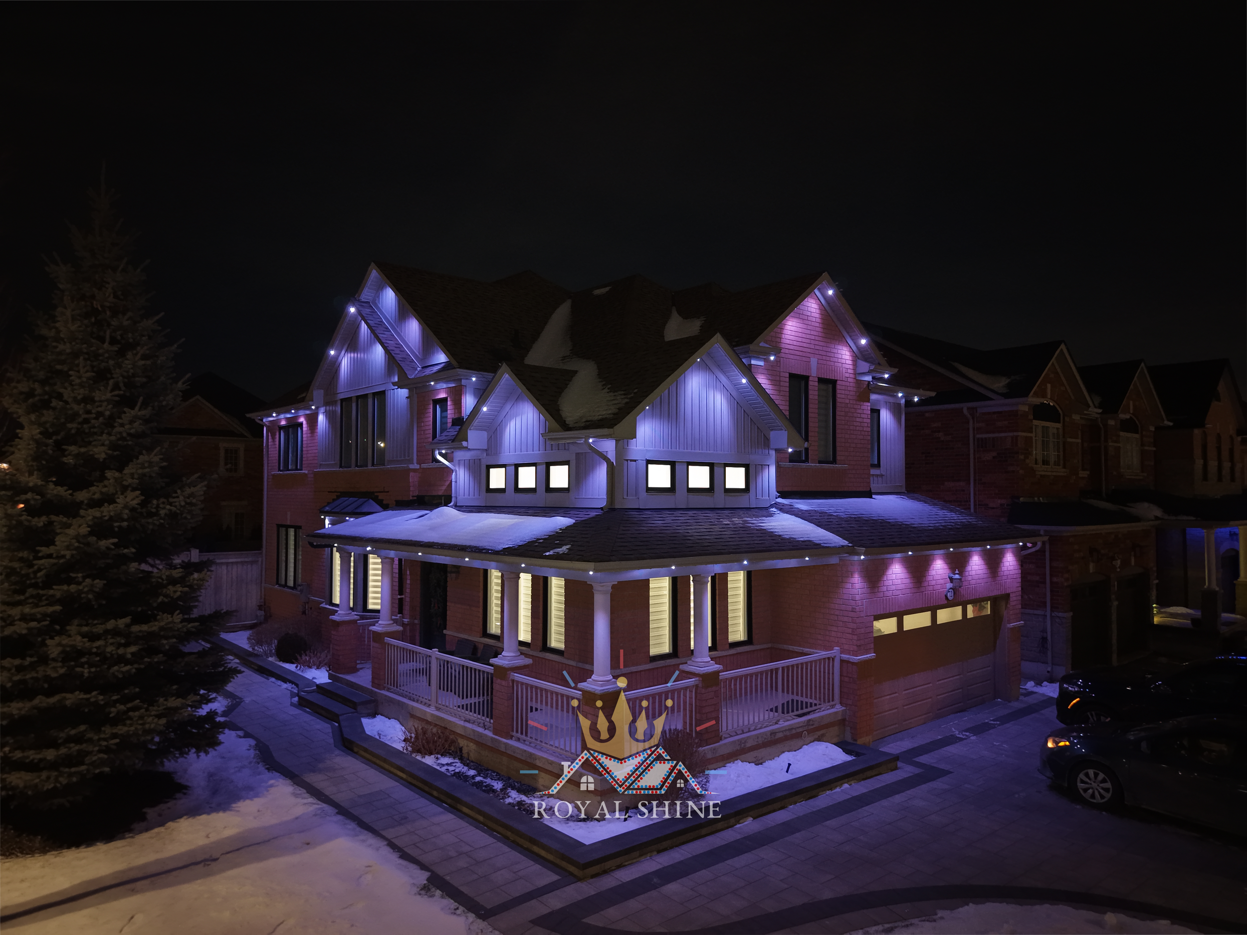 House with warm white LED pot lights, brick exterior, two-car garage, and porch at night.