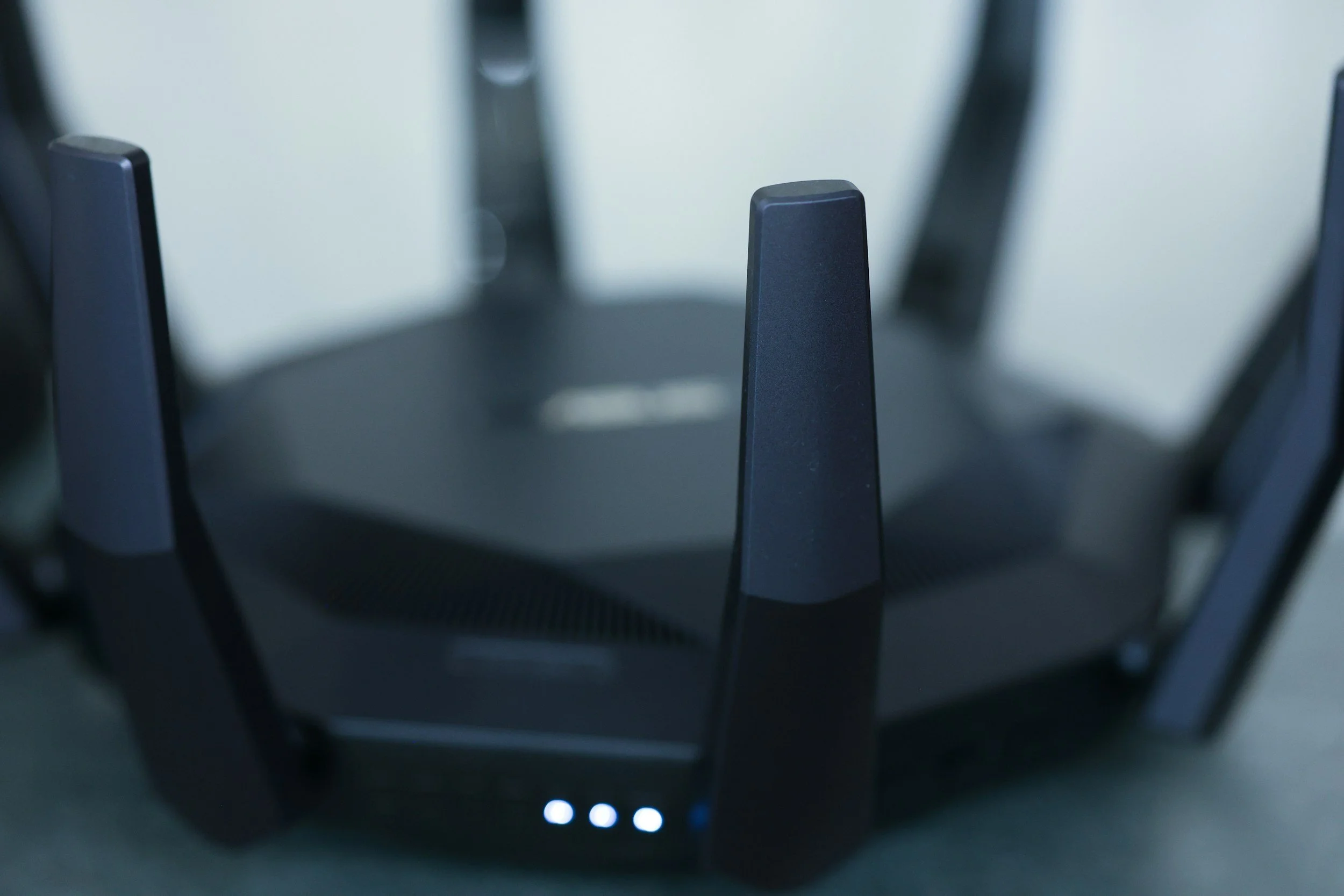 Close-up of a black Wi-Fi router with antennas, showing the illuminated LED lights at the base.