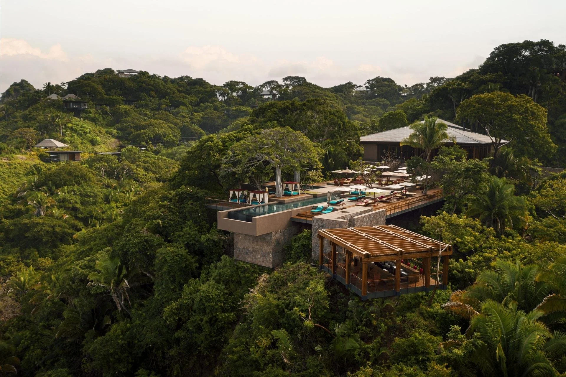 Luxury resort nestled in lush tropical forest with infinity pool and lounge area.