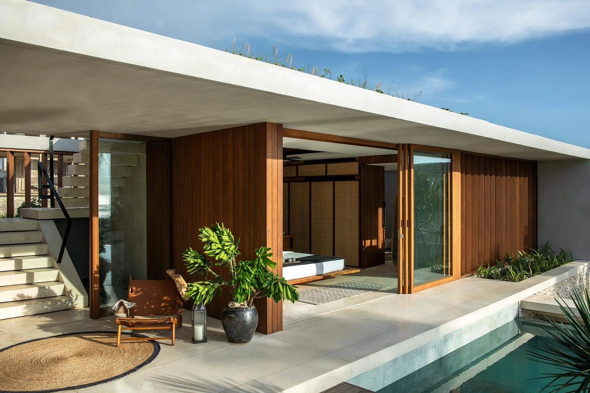 Modern house with wooden panels and glass, featuring an open patio area with potted plants and a small pool.