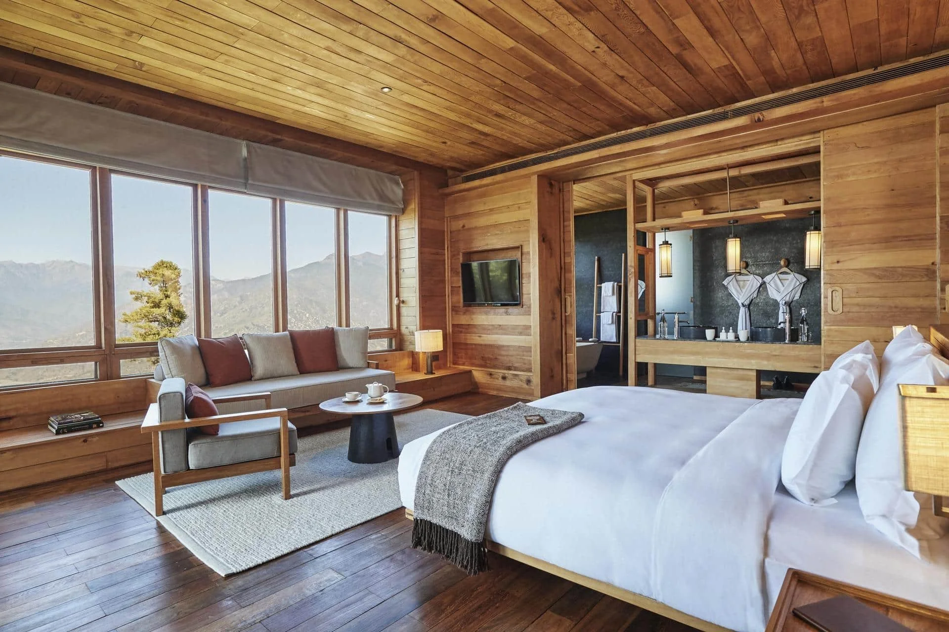 Luxury hotel room with wooden interior, large bed, sitting area, and mountain view from large windows.
